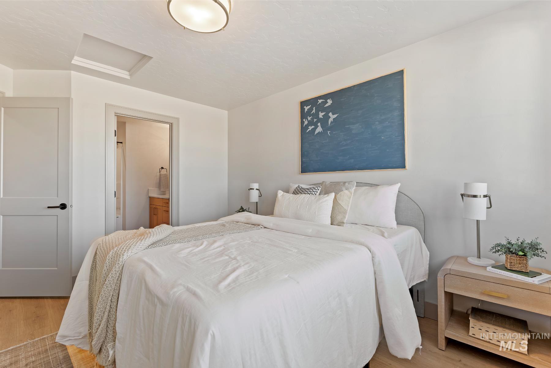 Bedroom featuring attic access, light wood-style flooring, and ensuite bath