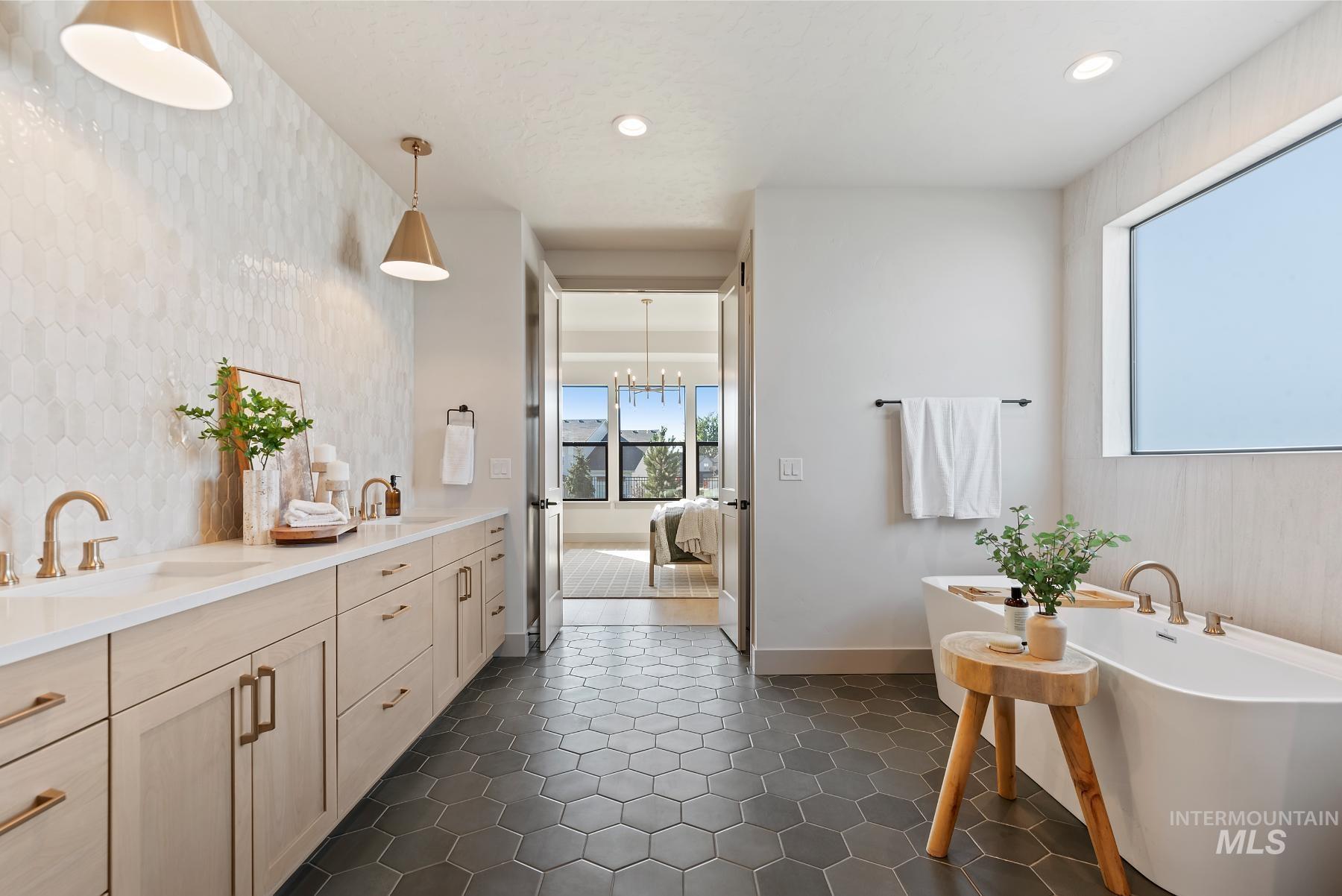 Ensuite bathroom featuring a freestanding bath, double vanity, recessed lighting, a chandelier, and dark tile patterned flooring