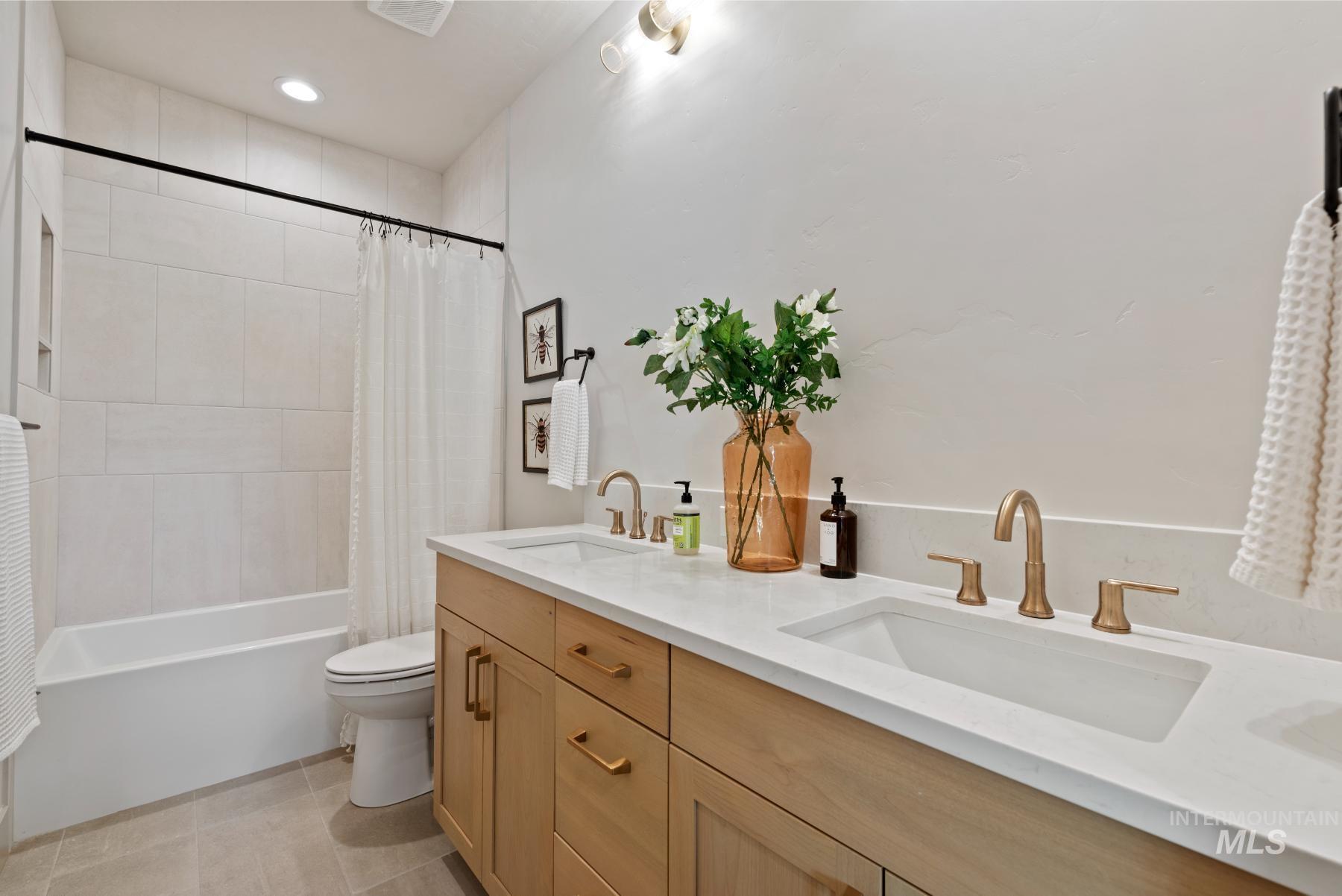 Full bathroom with double vanity, shower / bath combination with curtain, and light tile patterned floors