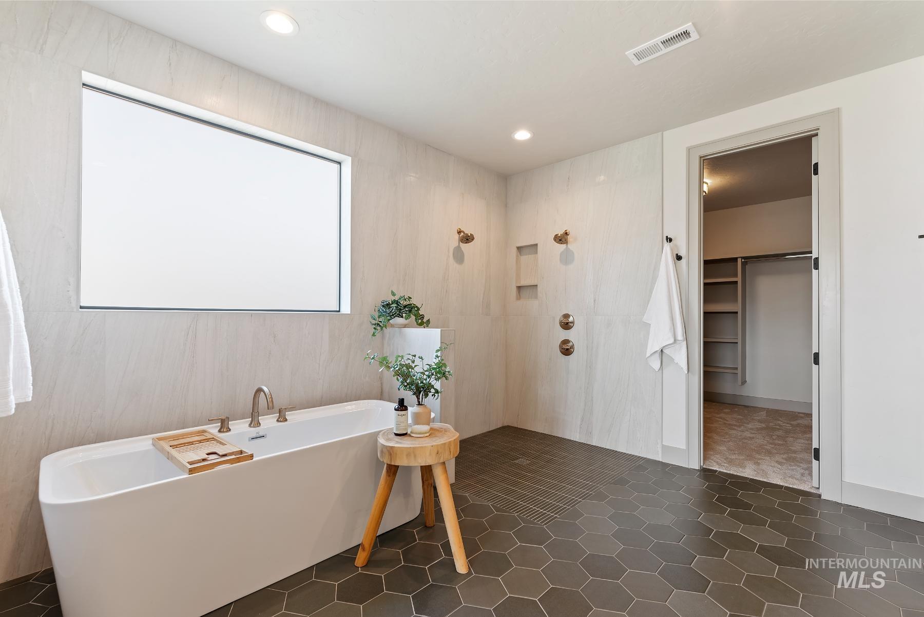 Full bathroom with a tile shower, a freestanding bath, a spacious closet, dark tile patterned floors, and recessed lighting