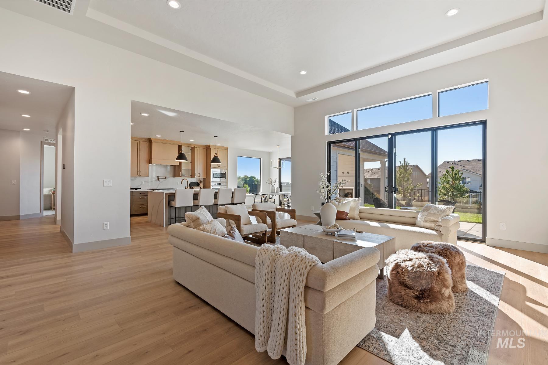 Living area featuring a tray ceiling, recessed lighting, light wood finished floors, and a high ceiling