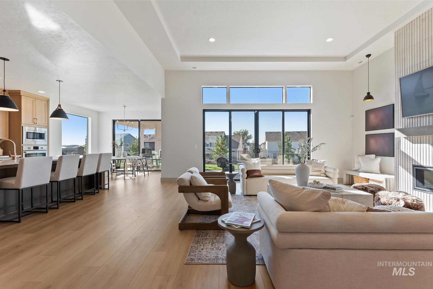 Living room featuring light wood-style flooring, a fireplace, a towering ceiling, recessed lighting, and a tray ceiling