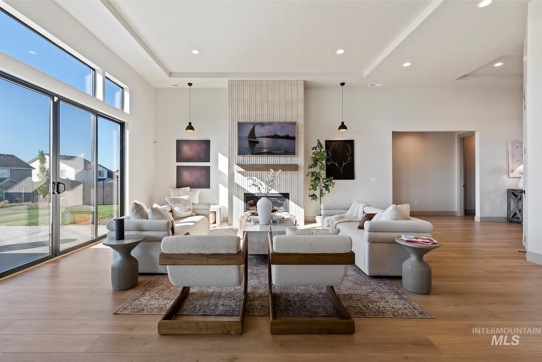 Living room featuring a raised ceiling, a fireplace, light wood finished floors, recessed lighting, and a towering ceiling