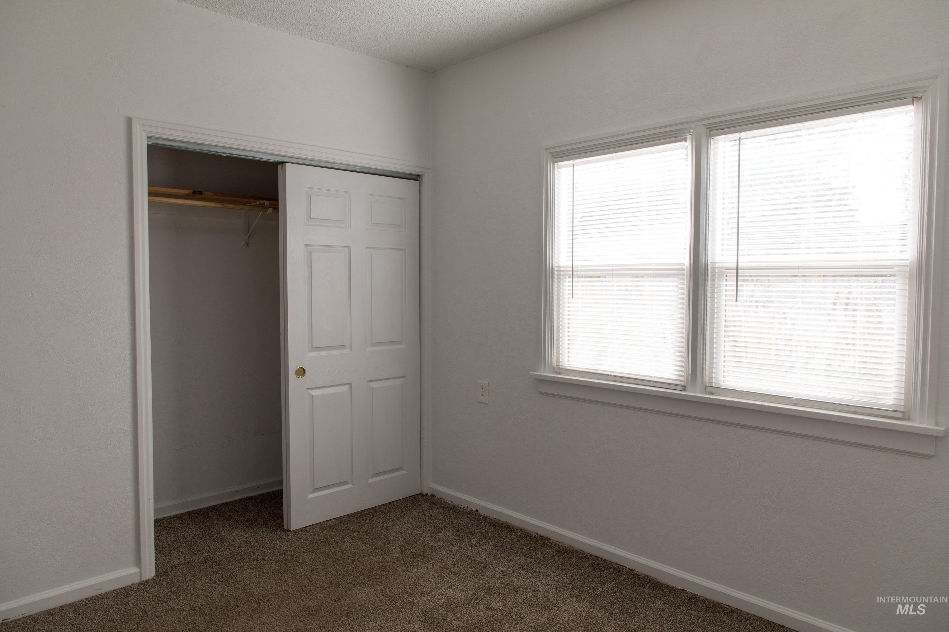 Unfurnished bedroom with dark colored carpet, a textured ceiling, and a closet