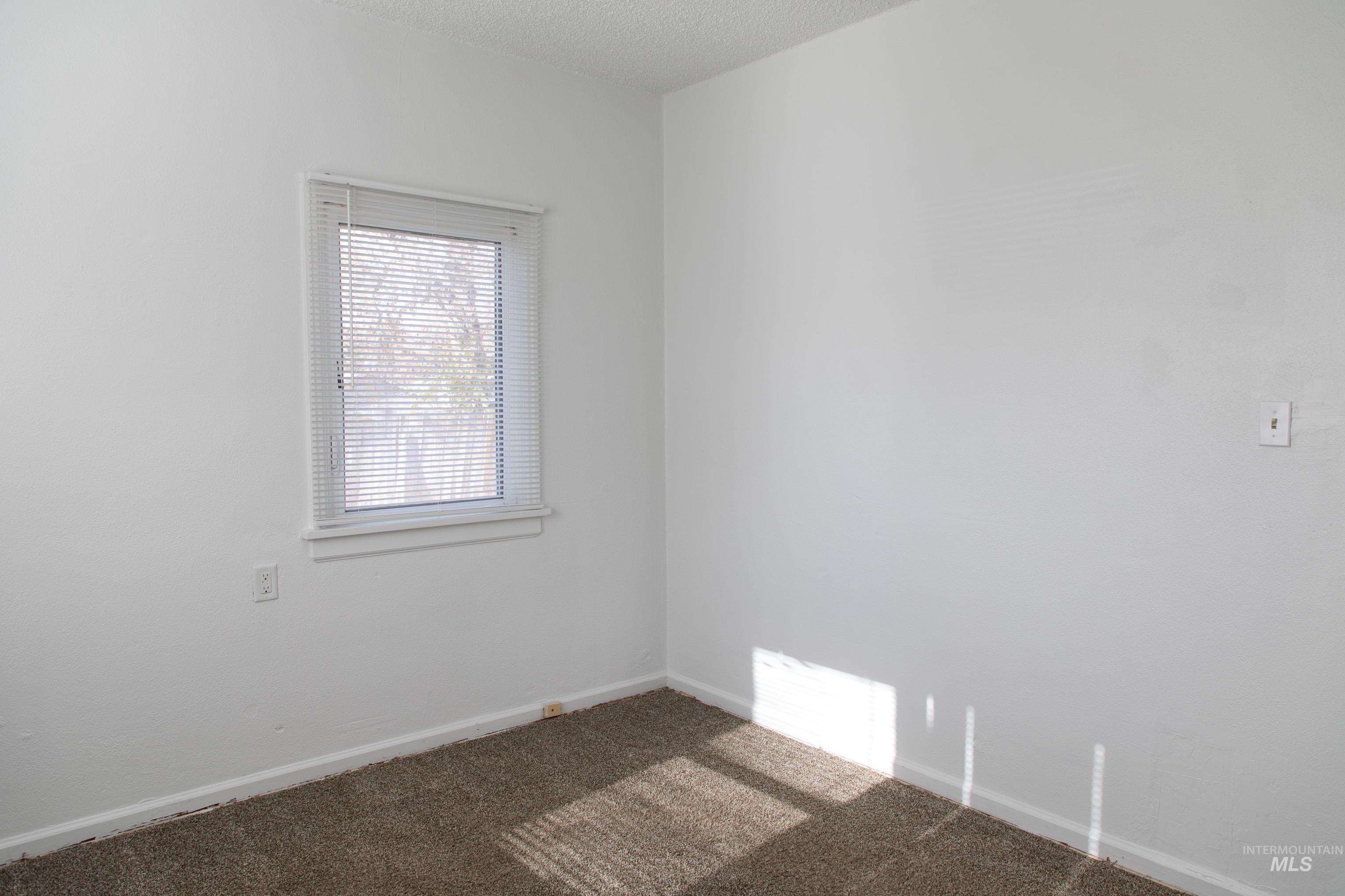 Carpeted empty room featuring a textured ceiling and baseboards