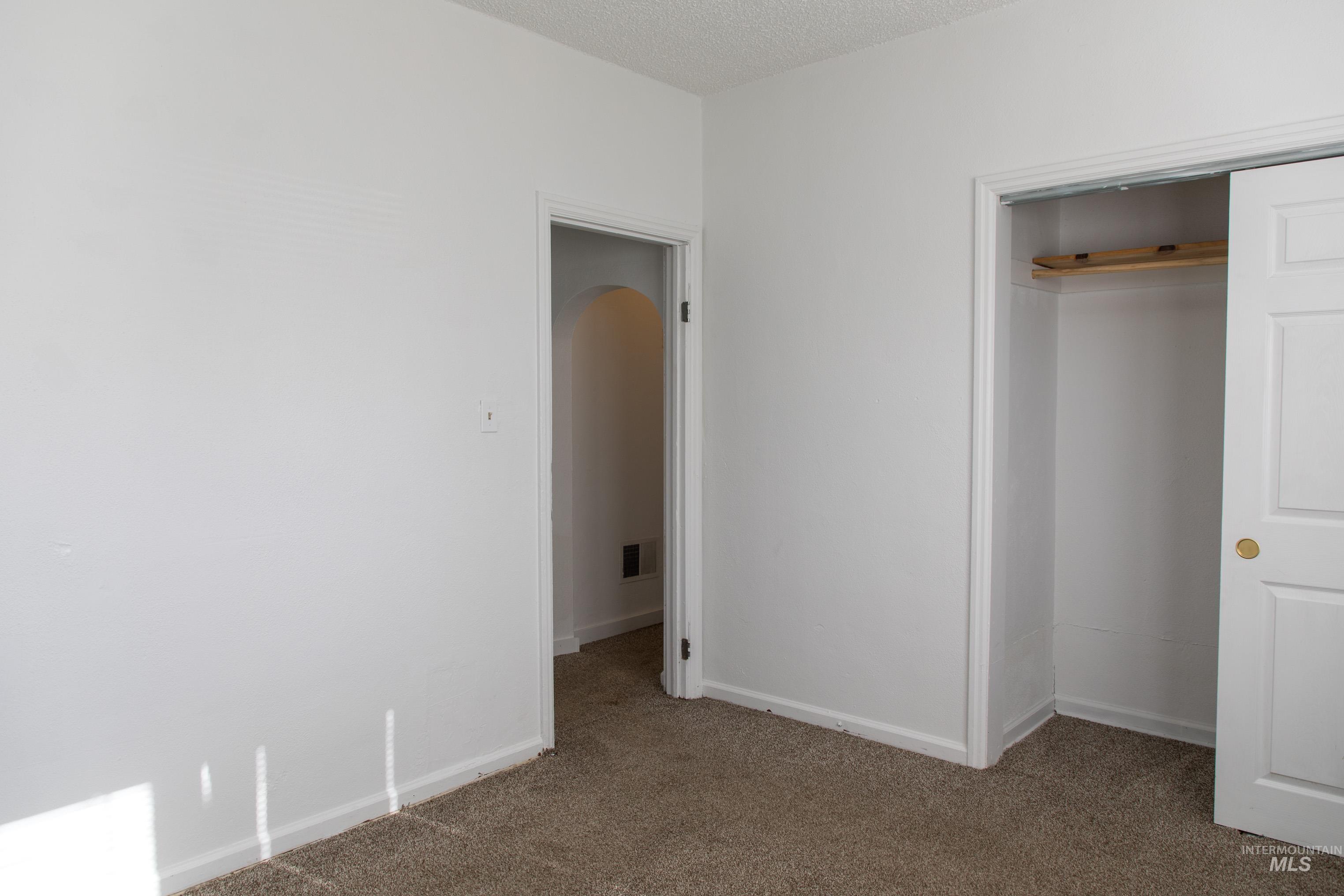 Unfurnished bedroom with light carpet, a textured ceiling, arched walkways, and a closet