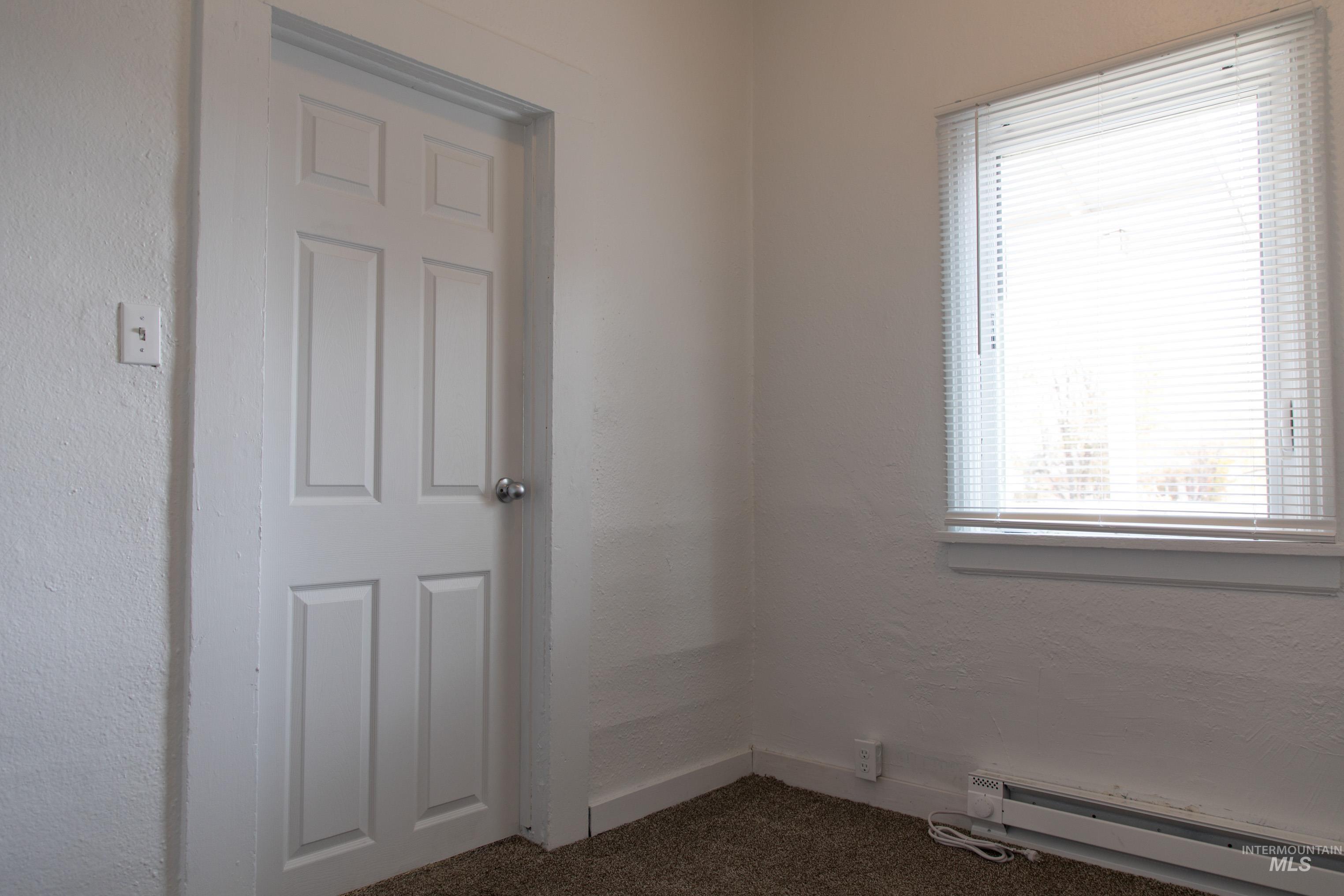 Spare room featuring dark carpet, a baseboard radiator, and a textured wall