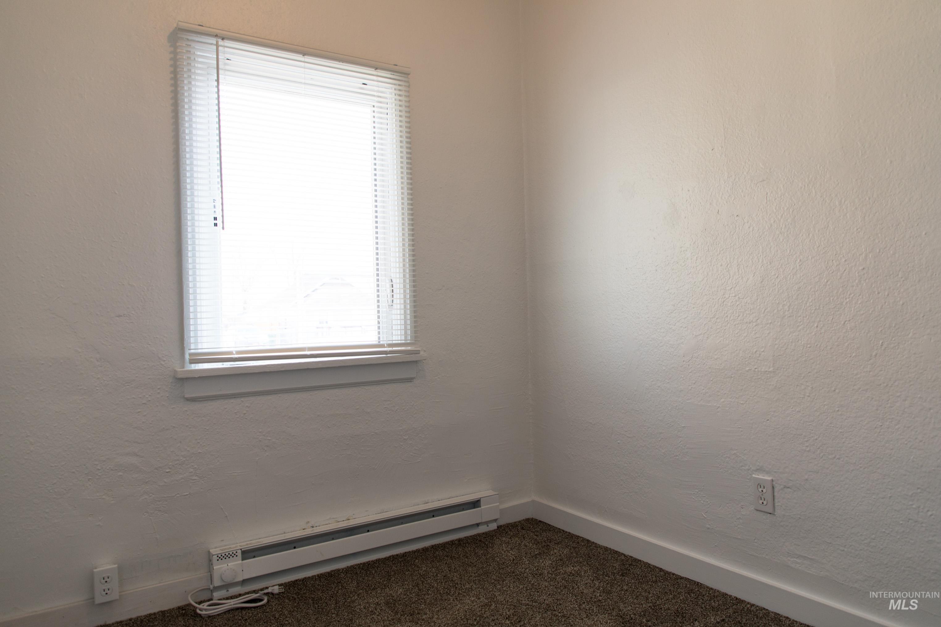 Empty room with a textured wall, a baseboard radiator, plenty of natural light, and dark colored carpet