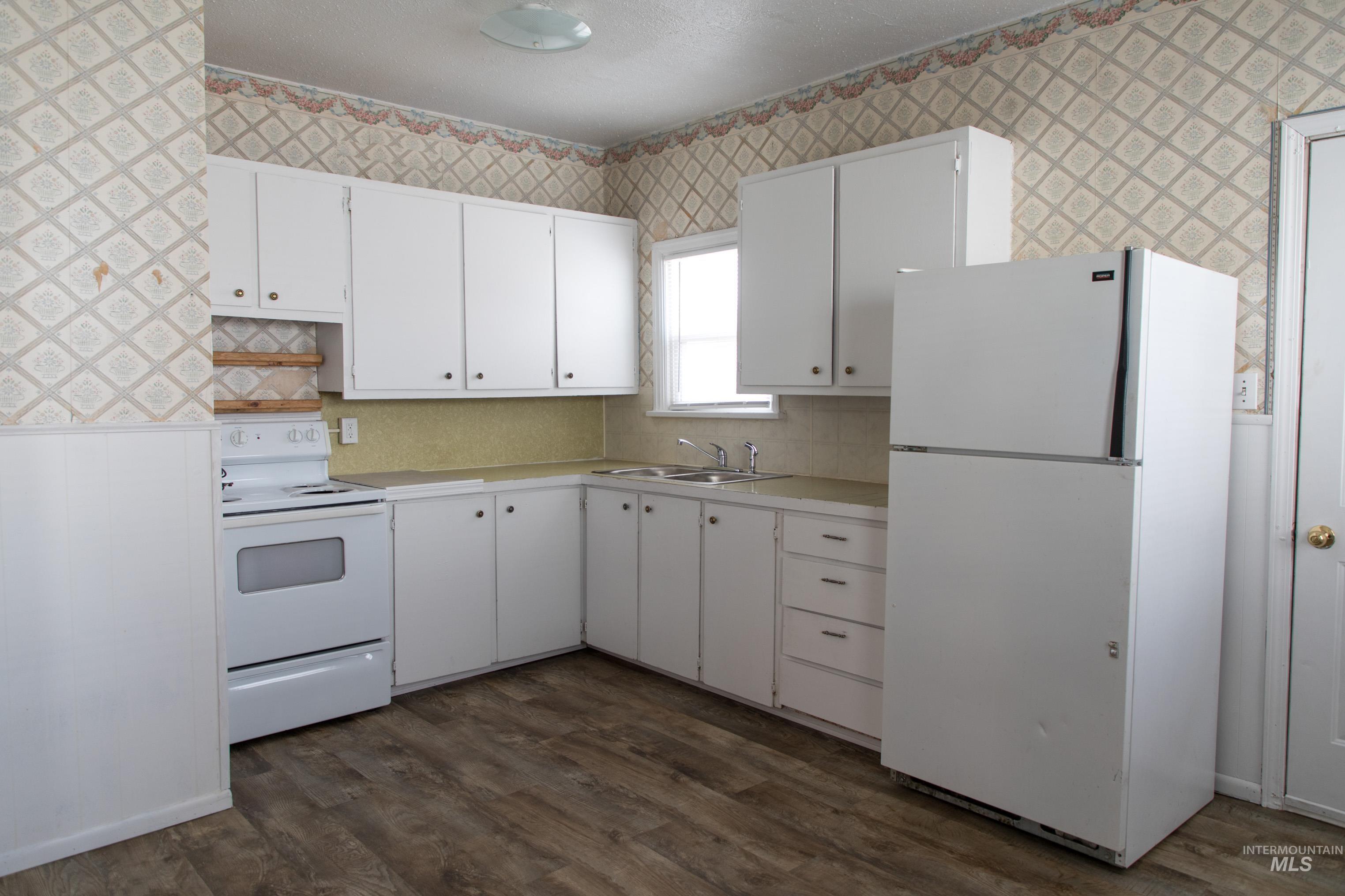 Kitchen with white appliances, wallpapered walls, light countertops, white cabinetry, and dark wood-type flooring