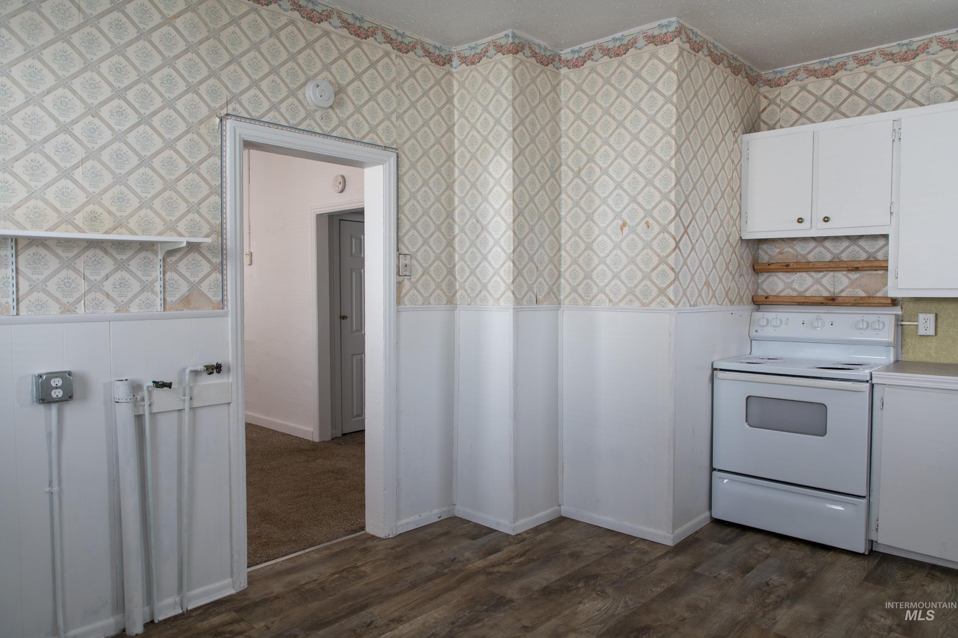 Kitchen featuring white range with electric stovetop, white cabinetry, light countertops, dark wood-style flooring, and wallpapered walls
