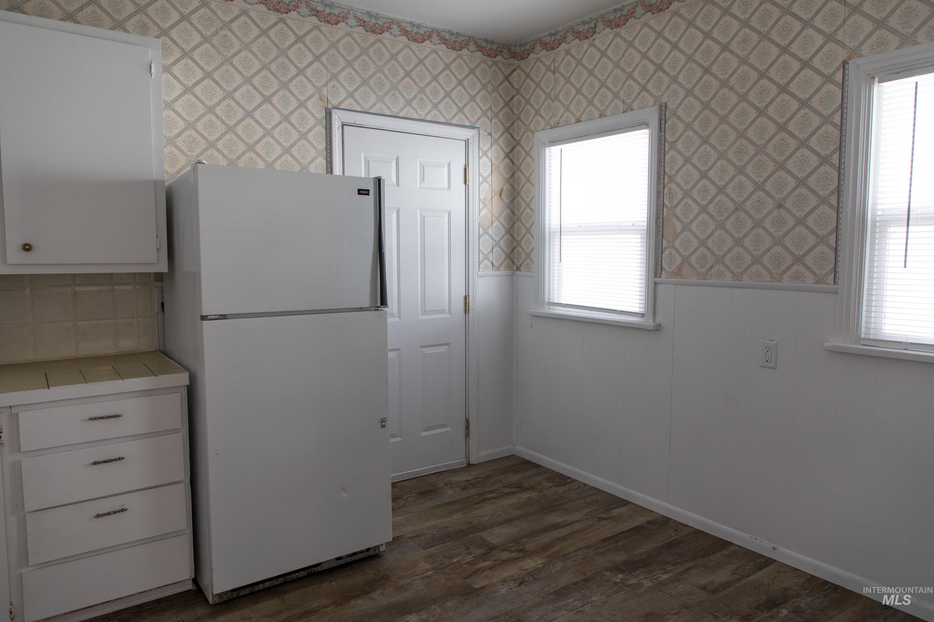 Kitchen with white cabinets, freestanding refrigerator, a wainscoted wall, dark wood finished floors, and tile countertops