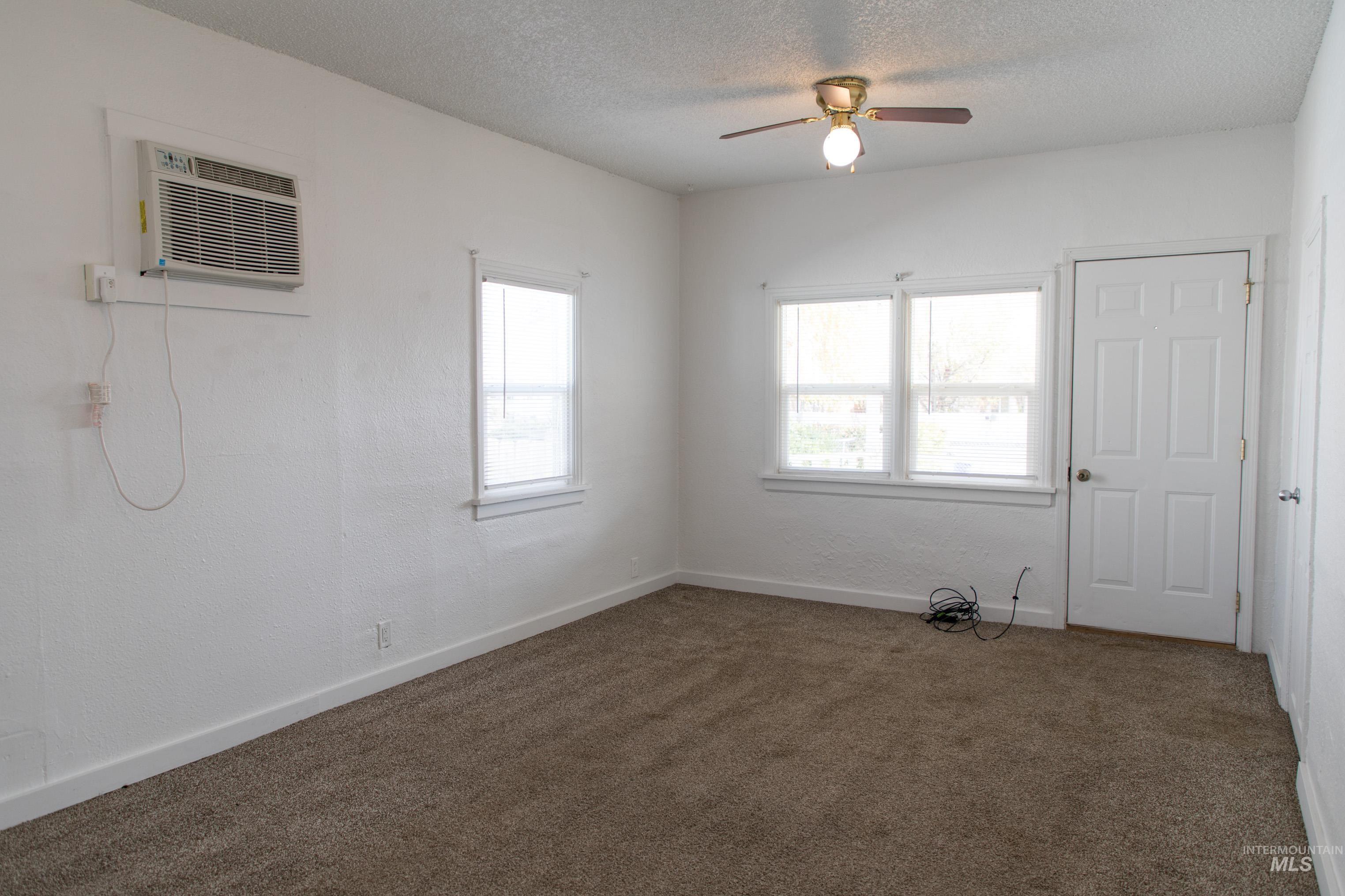 Unfurnished room featuring carpet floors, a textured ceiling, a ceiling fan, a textured wall, and a wall mounted AC