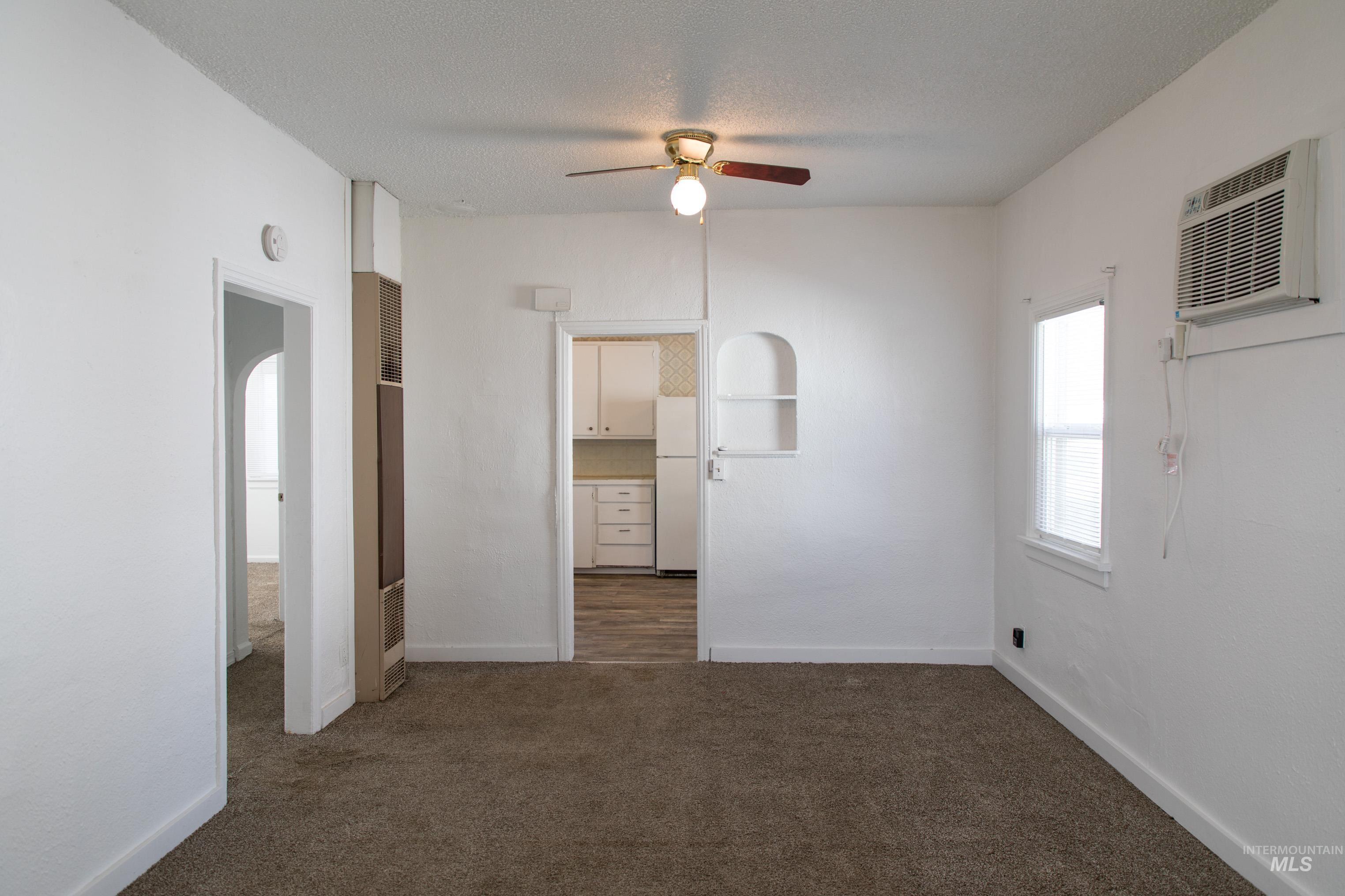 Unfurnished bedroom featuring dark colored carpet, freestanding refrigerator, ceiling fan, a wall mounted AC, and a heating unit