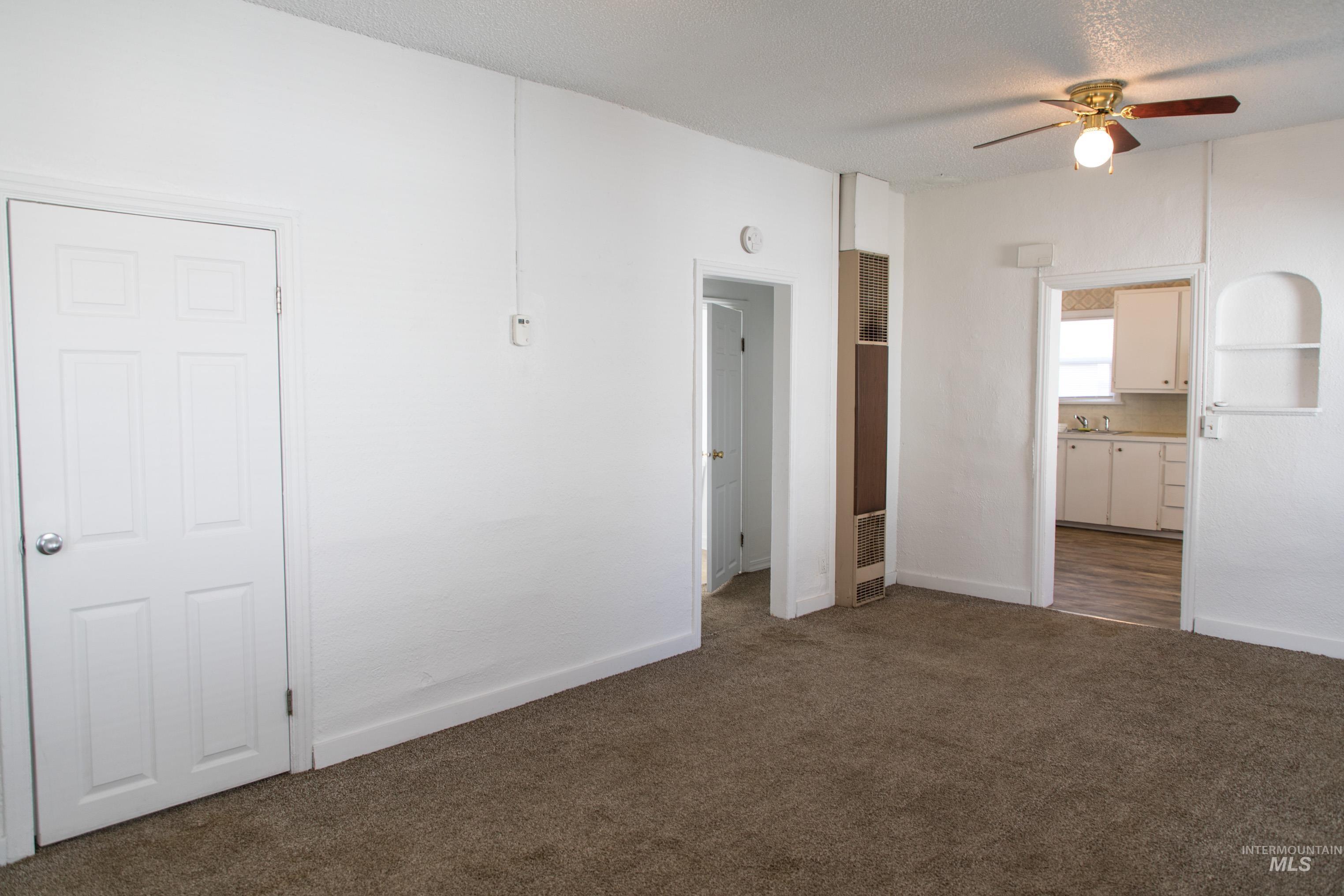 Unfurnished bedroom with dark colored carpet, ceiling fan, and a heating unit