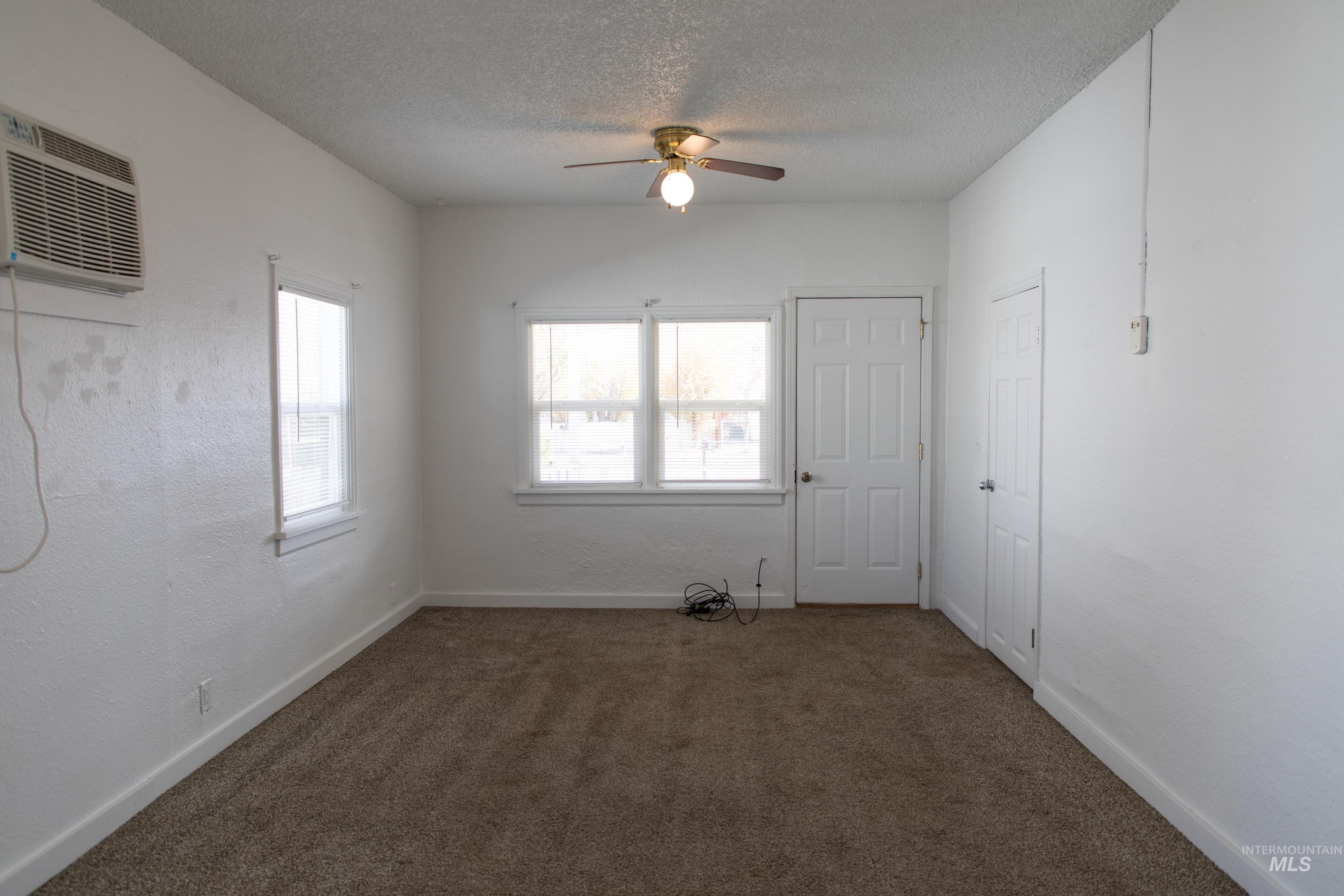 Spare room with dark carpet, a textured ceiling, an AC wall unit, a ceiling fan, and a textured wall