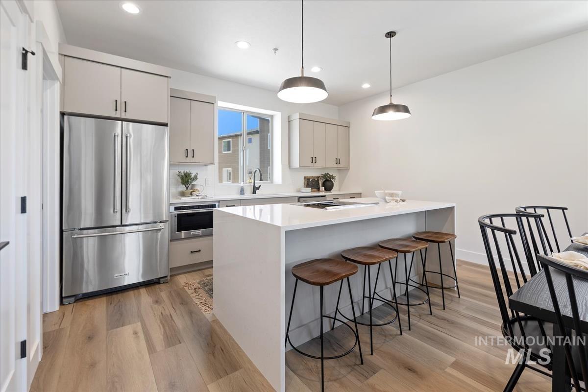 Kitchen featuring stainless steel appliances, pendant lighting, light wood-style floors, light stone counters, and recessed lighting