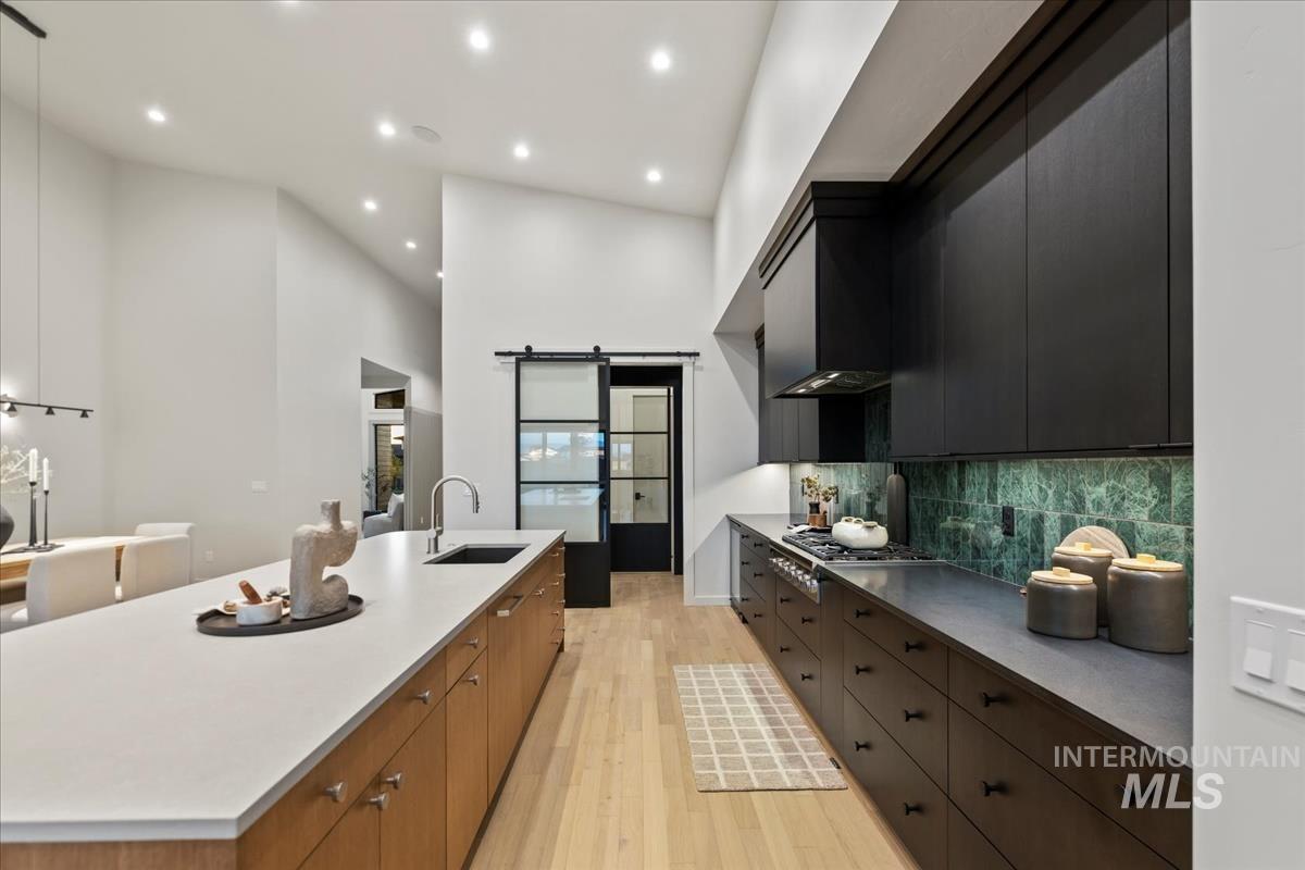 Kitchen with a barn door, light wood finished floors, a towering ceiling, modern cabinets, and a large island with sink