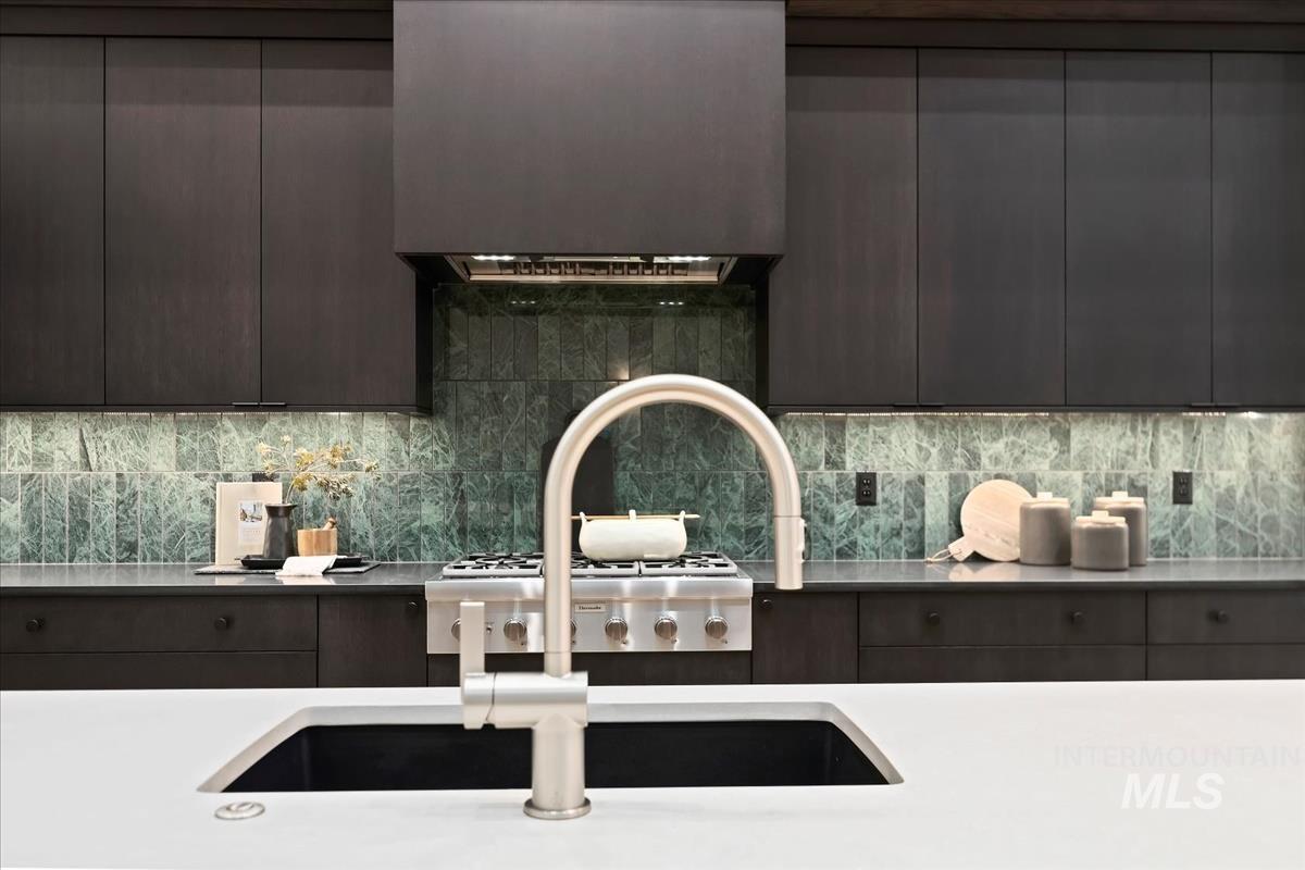 Kitchen featuring modern cabinets, dark cabinets, decorative backsplash, and light stone countertops