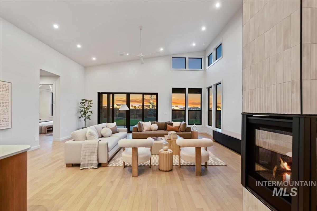 Living area featuring a multi sided fireplace, light wood finished floors, recessed lighting, a high ceiling, and a ceiling fan