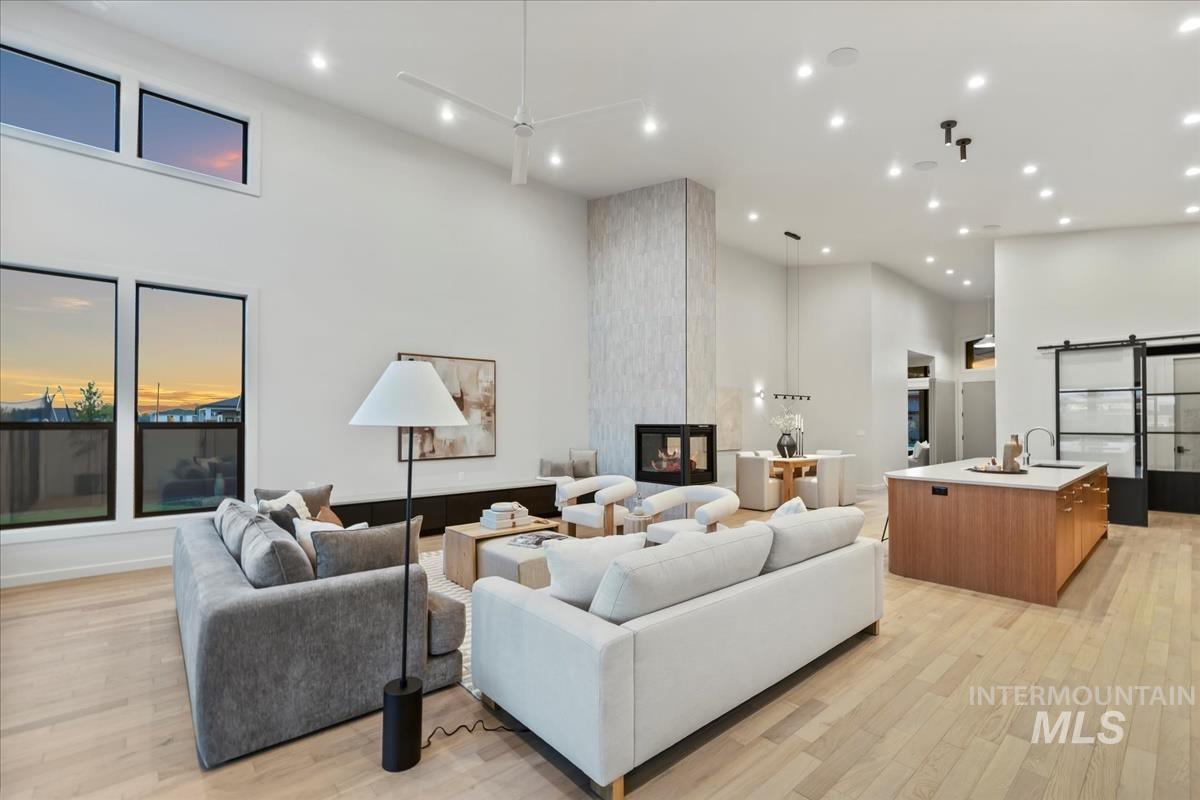 Living area featuring a towering ceiling, light wood-type flooring, a barn door, recessed lighting, and a multi sided fireplace