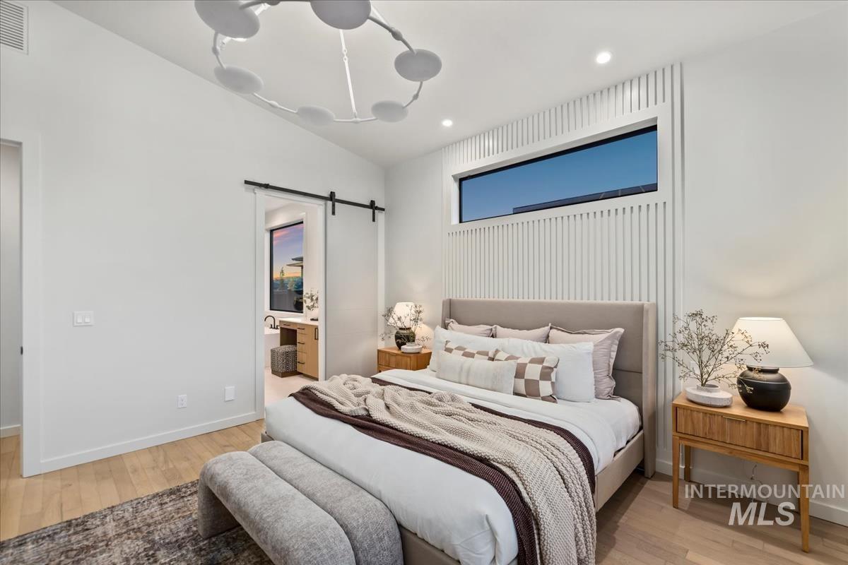 Bedroom featuring a barn door, light wood-style flooring, ensuite bath, and recessed lighting