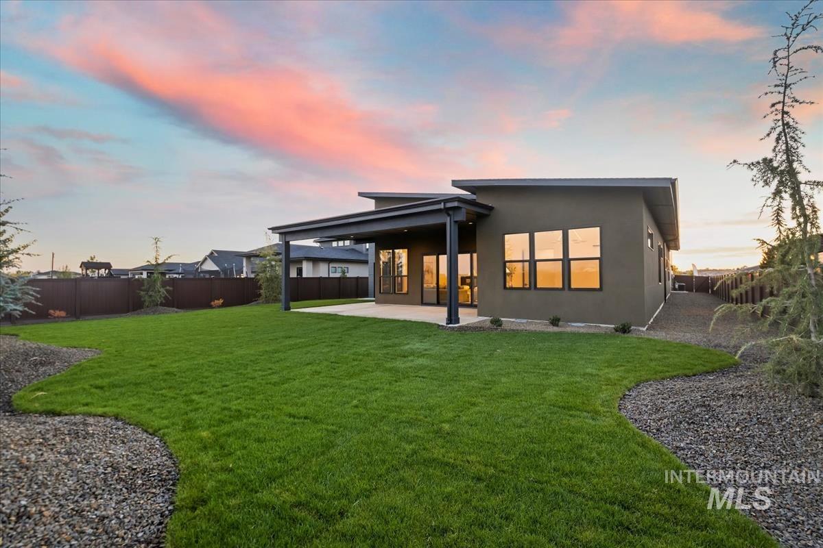 Back of property at dusk with a fenced backyard, stucco siding, and a large, covered patio area