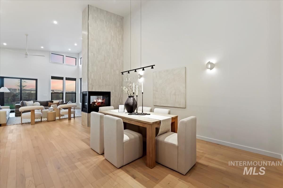 Dining space featuring light wood-style flooring, a high ceiling, a multi sided fireplace, recessed lighting, and a ceiling fan