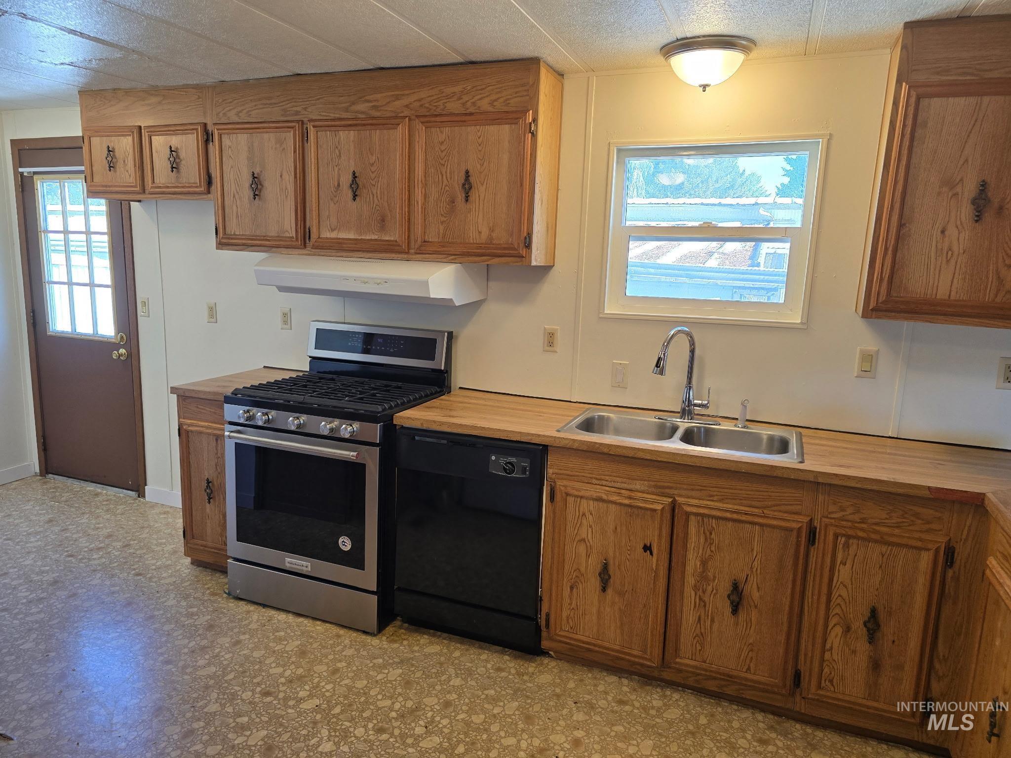 Kitchen featuring stainless steel gas range oven, black dishwasher, brown cabinetry, and plenty of natural light