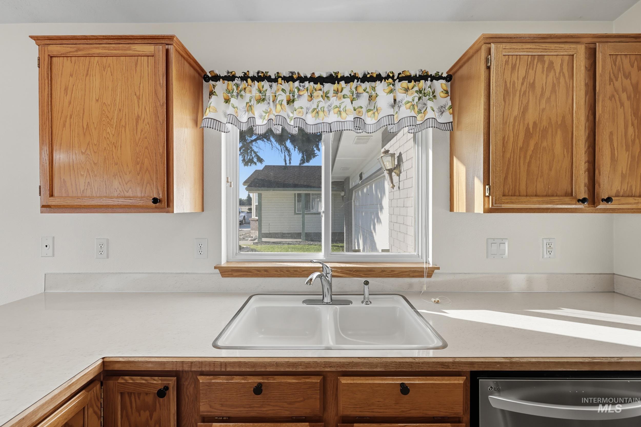Kitchen with light countertops, stainless steel dishwasher, and brown cabinetry