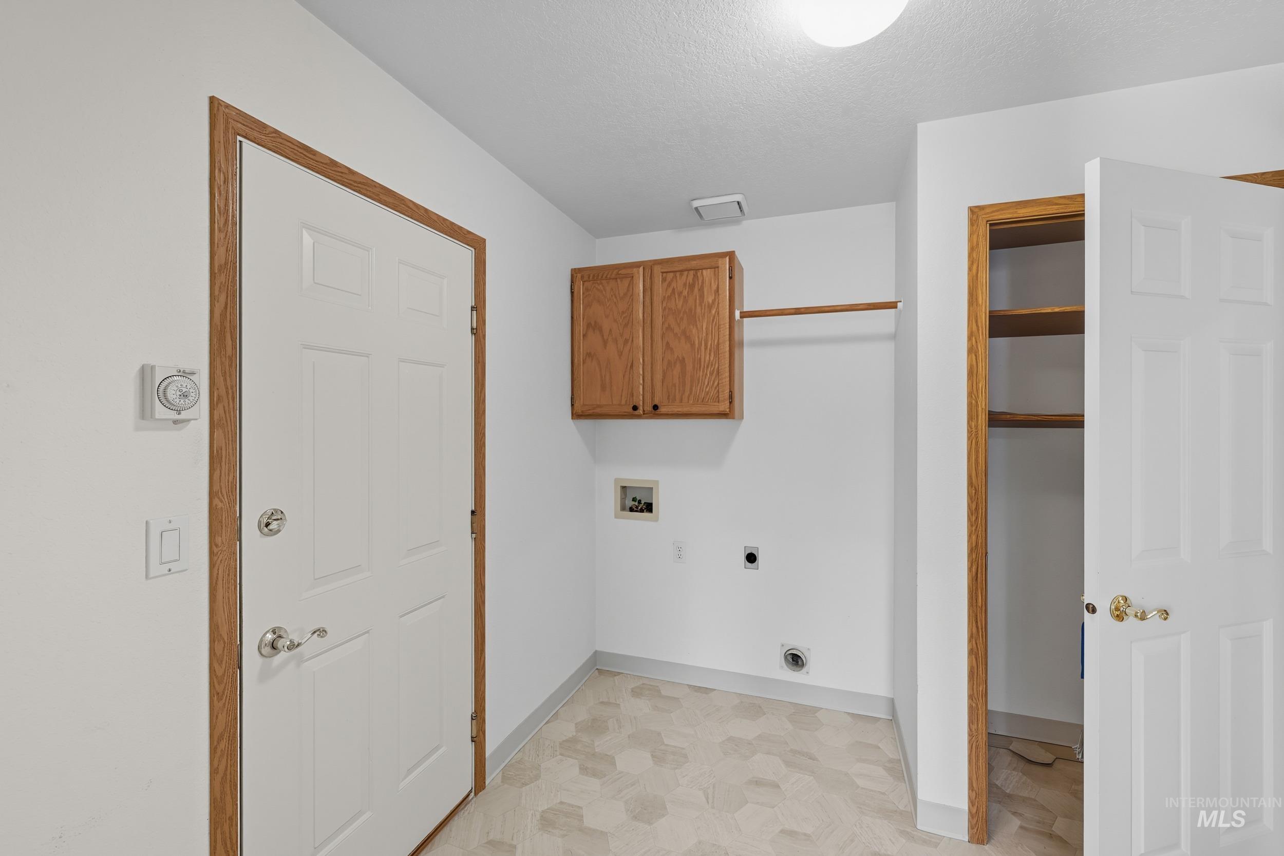 Laundry area with electric dryer hookup, washer hookup, cabinet space, and a textured ceiling