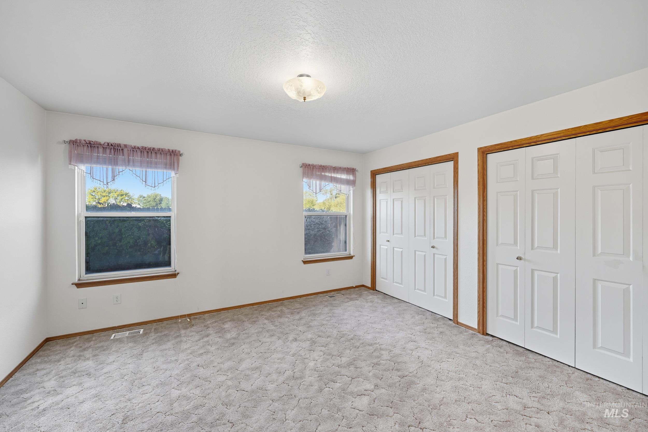 Unfurnished bedroom featuring two closets, carpet flooring, and a textured ceiling