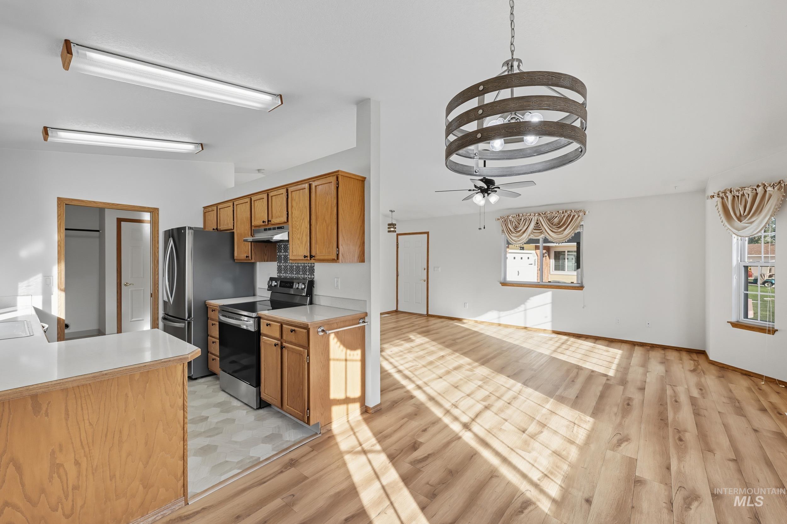 Kitchen with light countertops, electric range, brown cabinetry, light wood-style flooring, and a peninsula