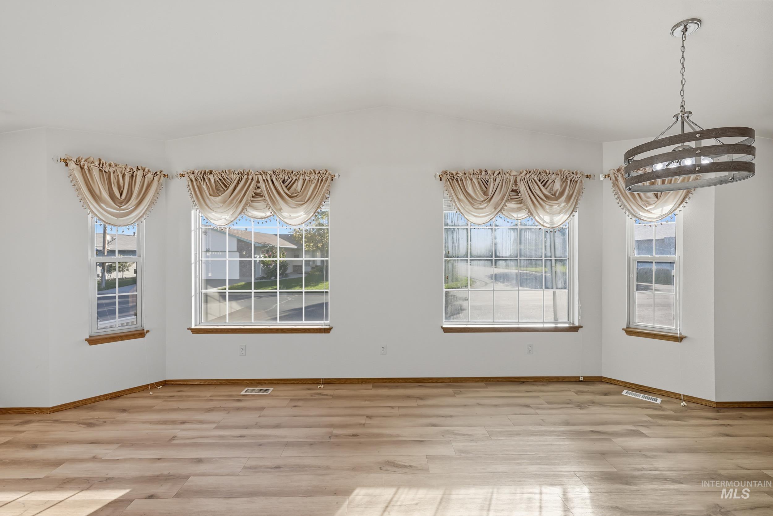 Unfurnished dining area featuring light wood finished floors, lofted ceiling, and a chandelier