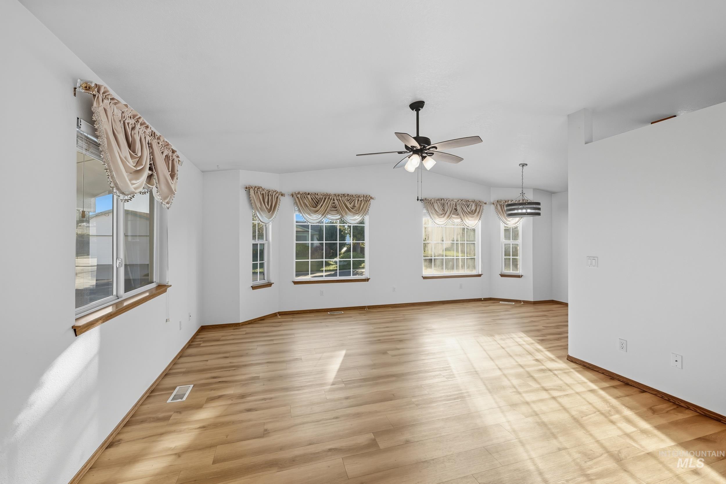 Empty room with light wood-type flooring, vaulted ceiling, and ceiling fan