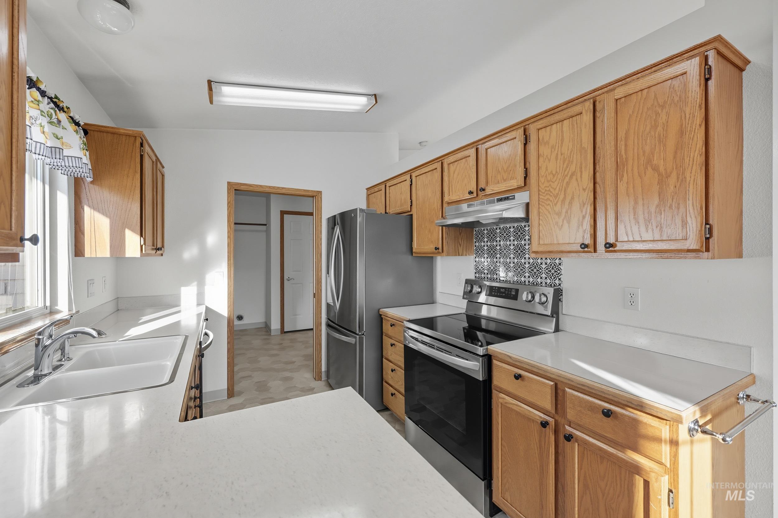Kitchen with stainless steel appliances, light countertops, backsplash, under cabinet range hood, and lofted ceiling