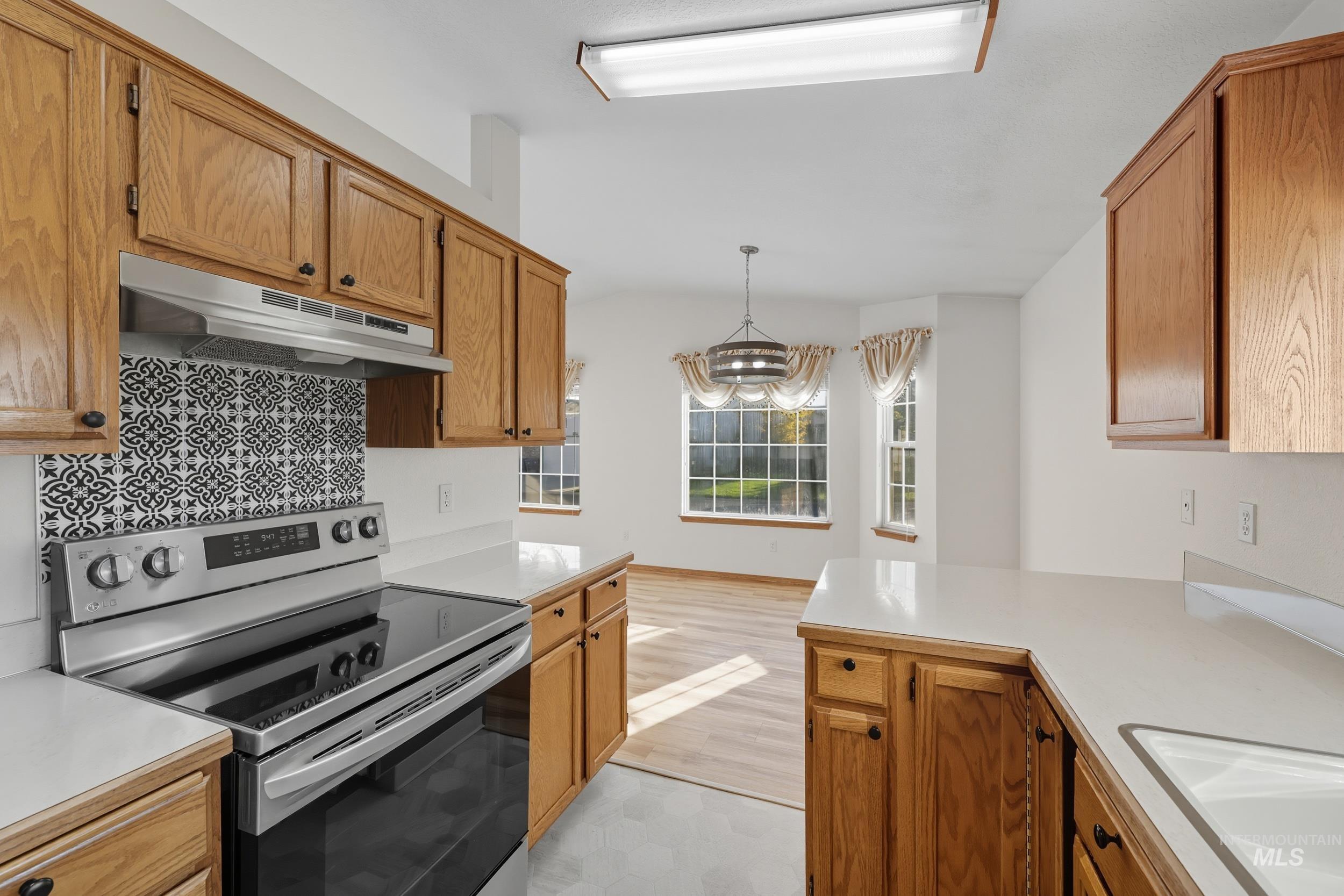 Kitchen featuring stainless steel range with electric stovetop, light countertops, under cabinet range hood, and brown cabinetry