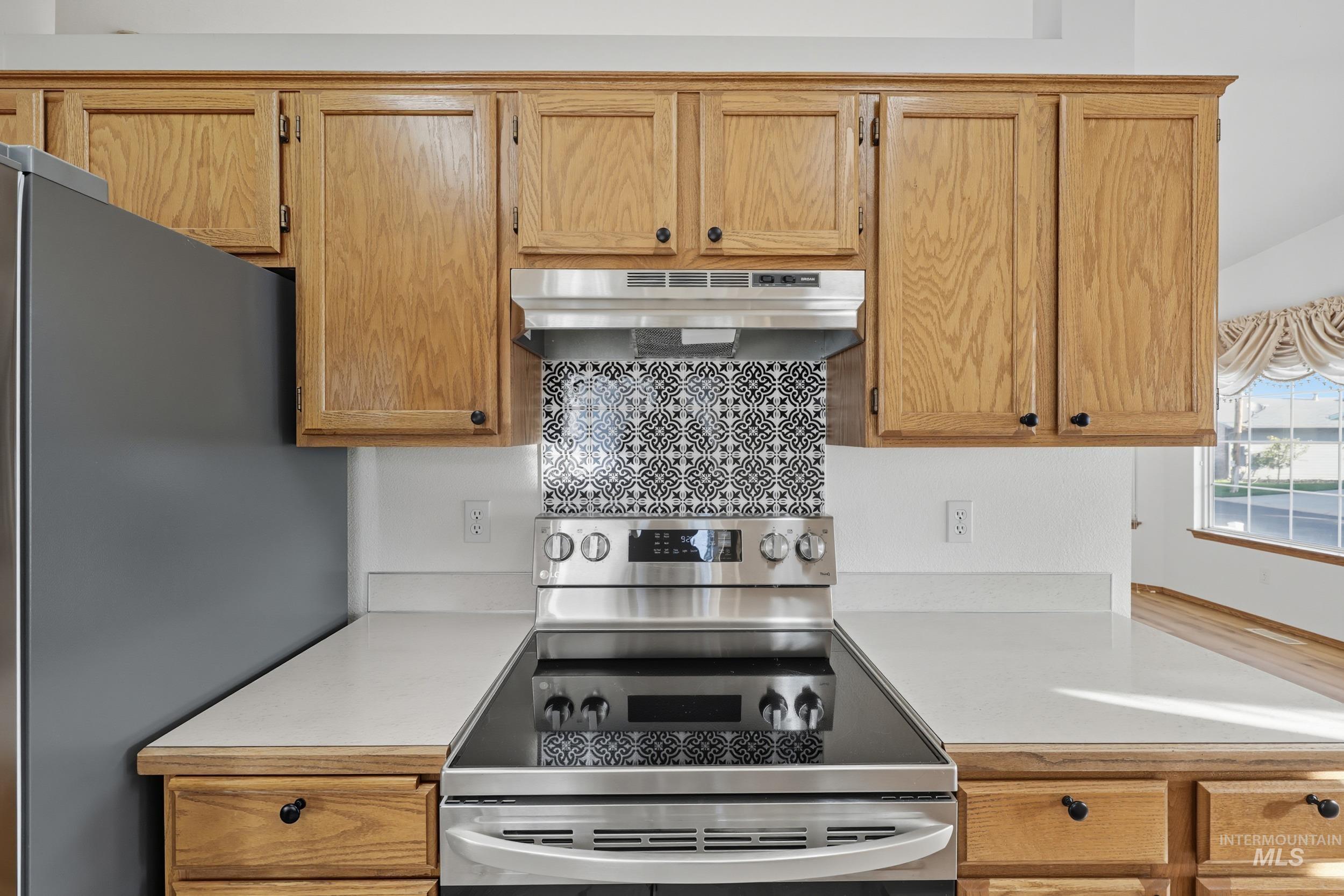 Kitchen with light countertops, stainless steel appliances, under cabinet range hood, and backsplash