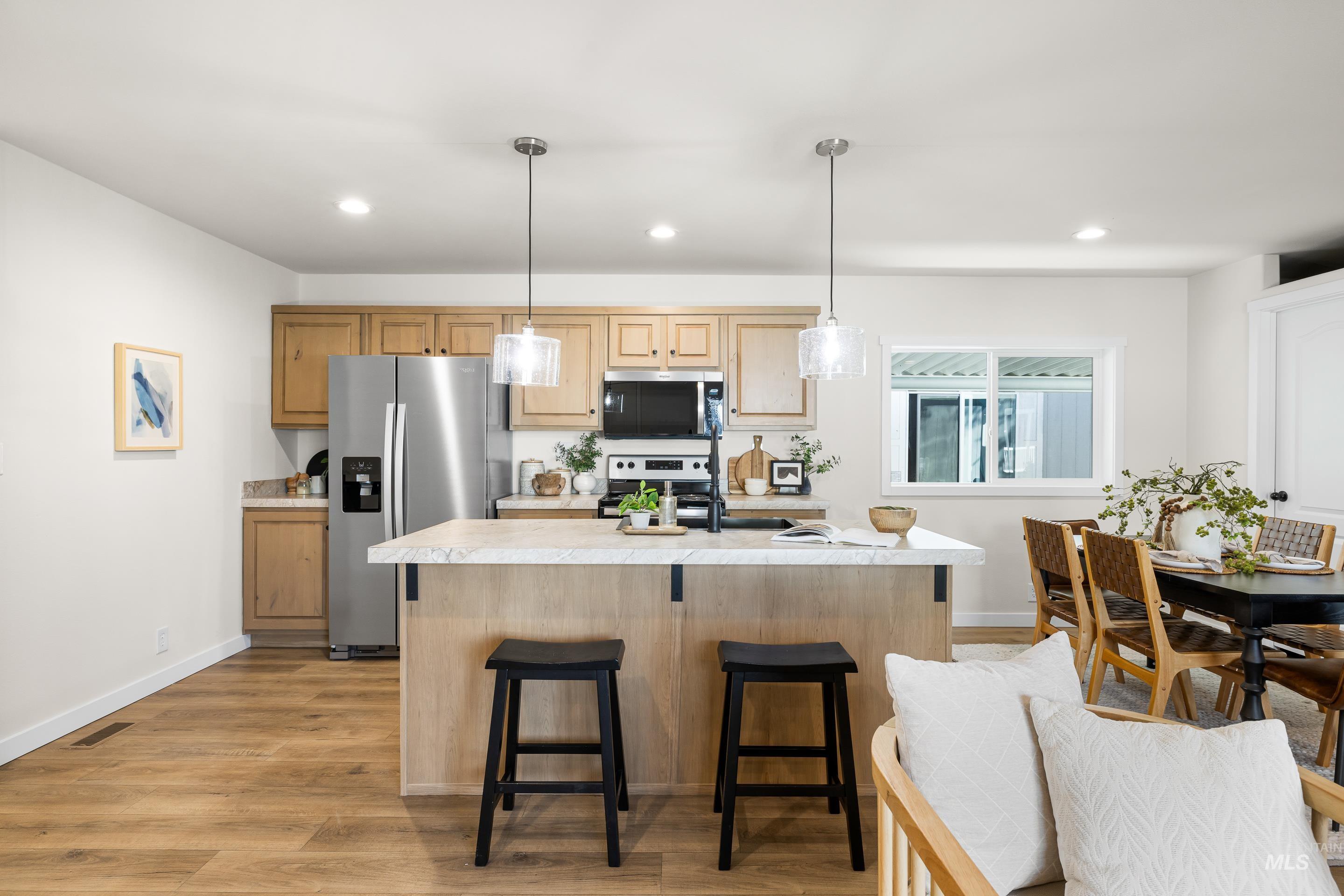 Kitchen featuring stainless steel appliances, decorative light fixtures, a kitchen breakfast bar, light countertops, and light wood finished floors