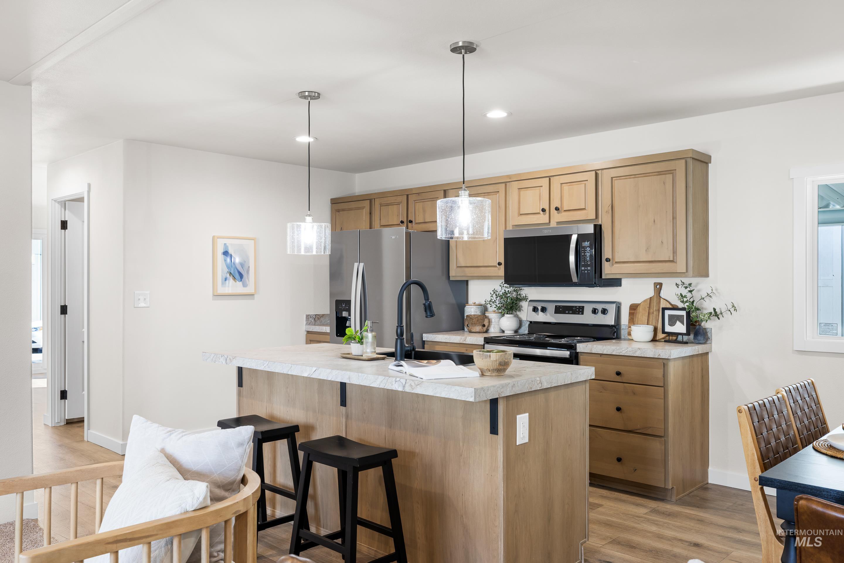 Kitchen featuring light countertops, hanging light fixtures, an island with sink, stainless steel appliances, and light wood-style flooring