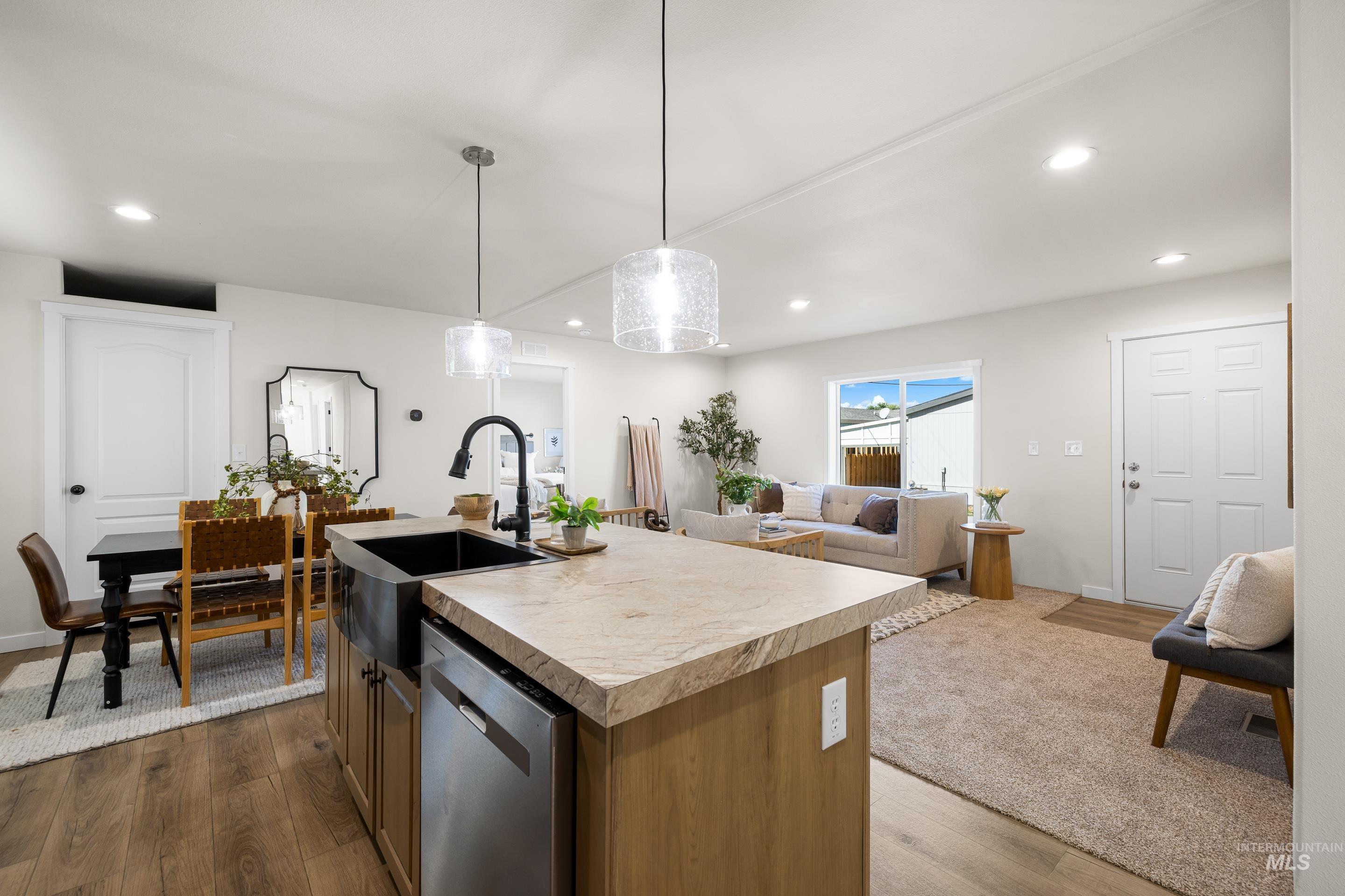 Kitchen featuring a center island with sink, light countertops, dark wood-style flooring, open floor plan, and stainless steel dishwasher