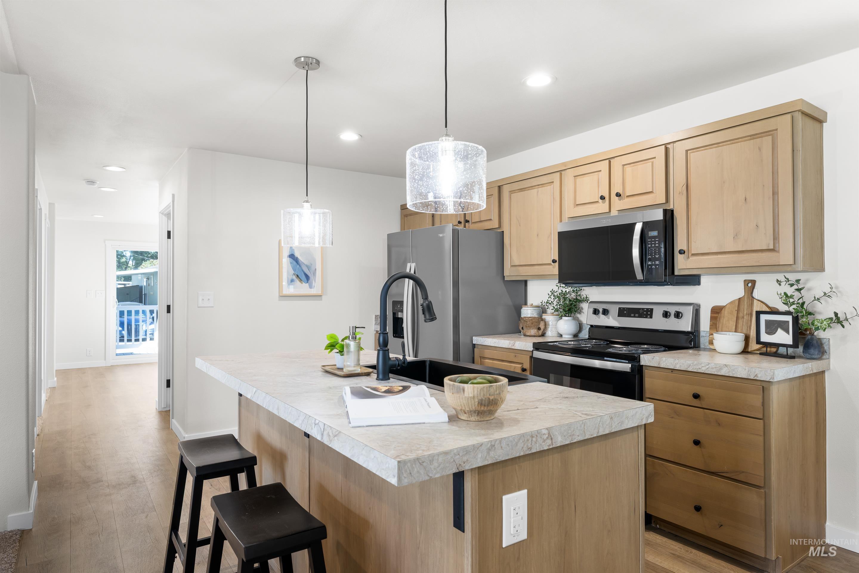 Kitchen with a breakfast bar, light brown cabinetry, light countertops, a center island with sink, and recessed lighting