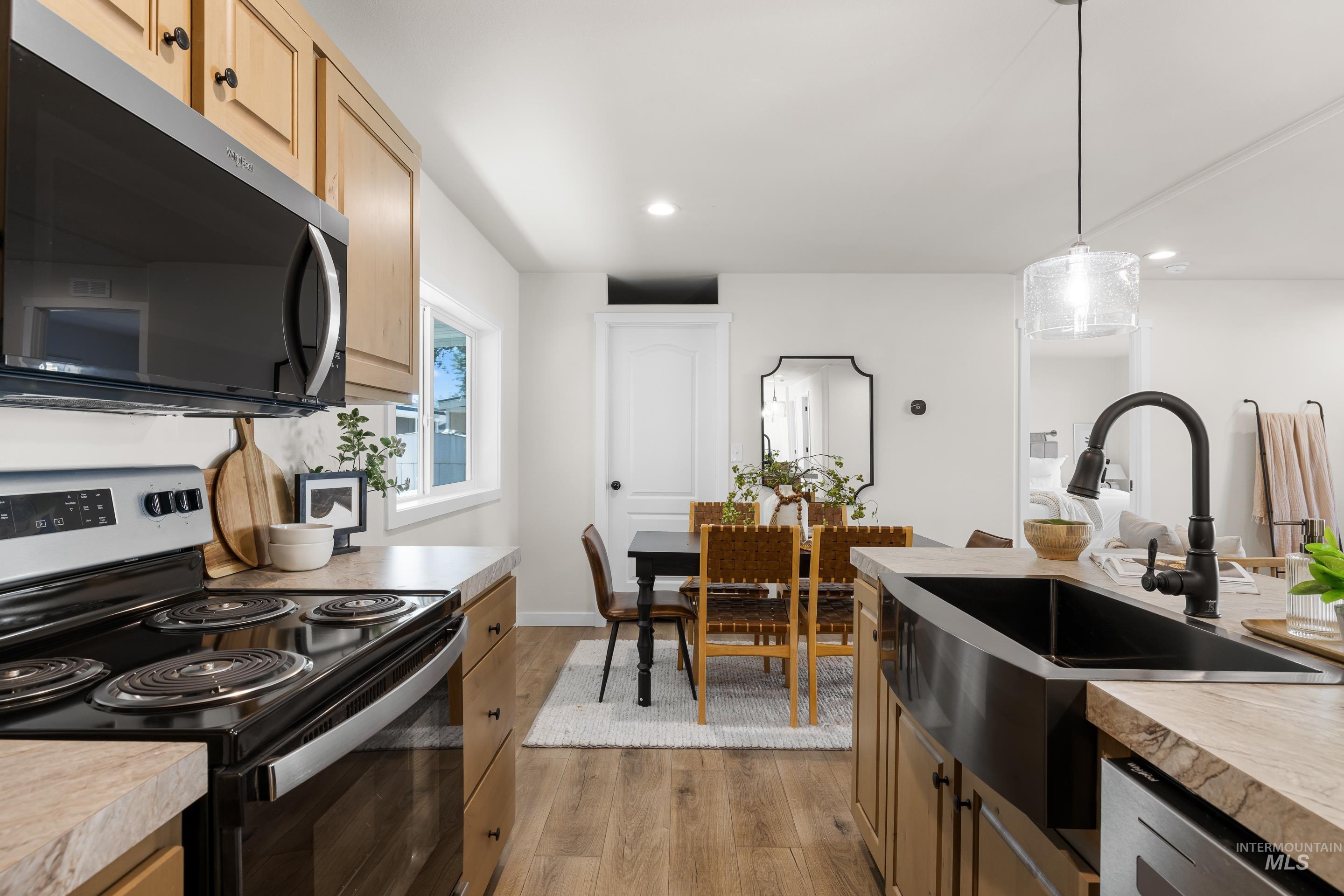 Kitchen with electric range oven, stainless steel microwave, light wood finished floors, light countertops, and pendant lighting