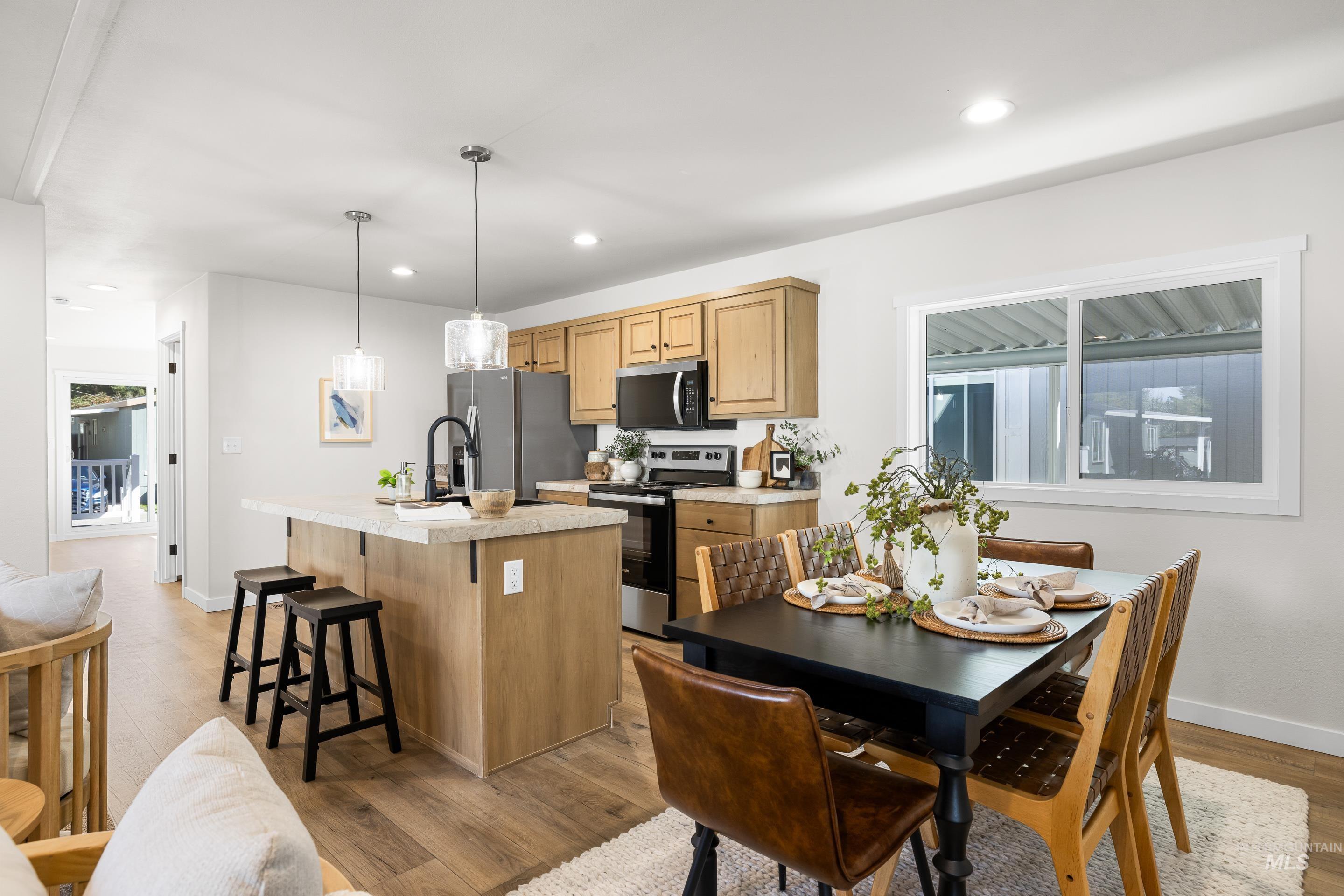 Kitchen featuring a kitchen bar, light countertops, stainless steel appliances, an island with sink, and light wood-style floors