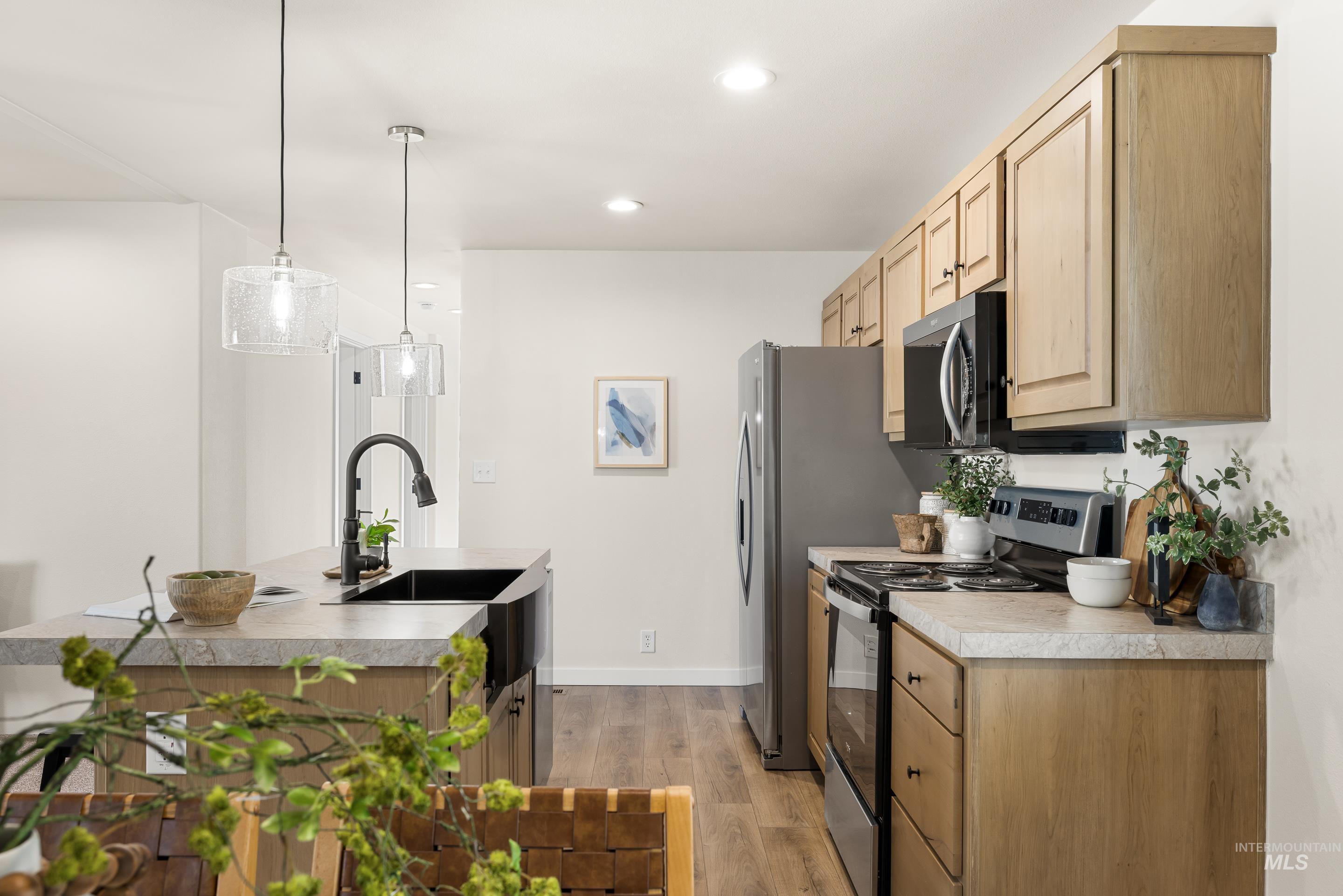 Kitchen featuring electric stove, light wood-style flooring, hanging light fixtures, a kitchen island with sink, and light brown cabinetry