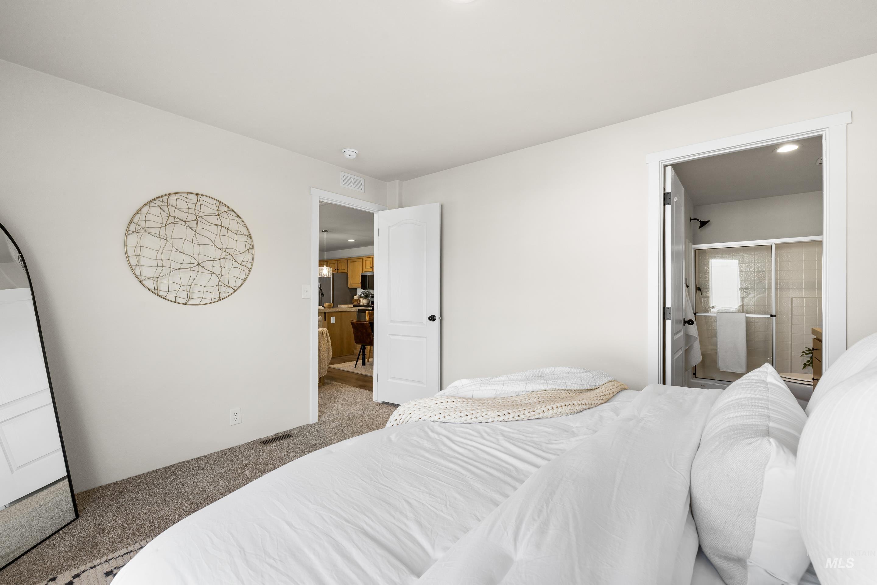 Carpeted bedroom with ensuite bathroom and freestanding refrigerator
