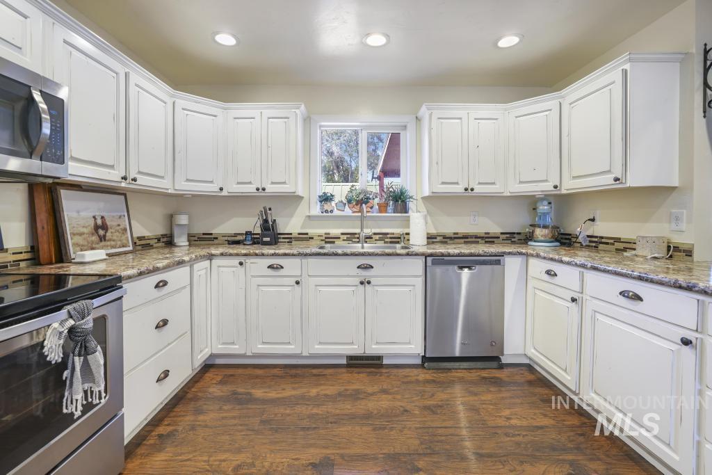 Kitchen with stainless steel appliances, white cabinets, light stone counters, dark wood-type flooring, and recessed lighting