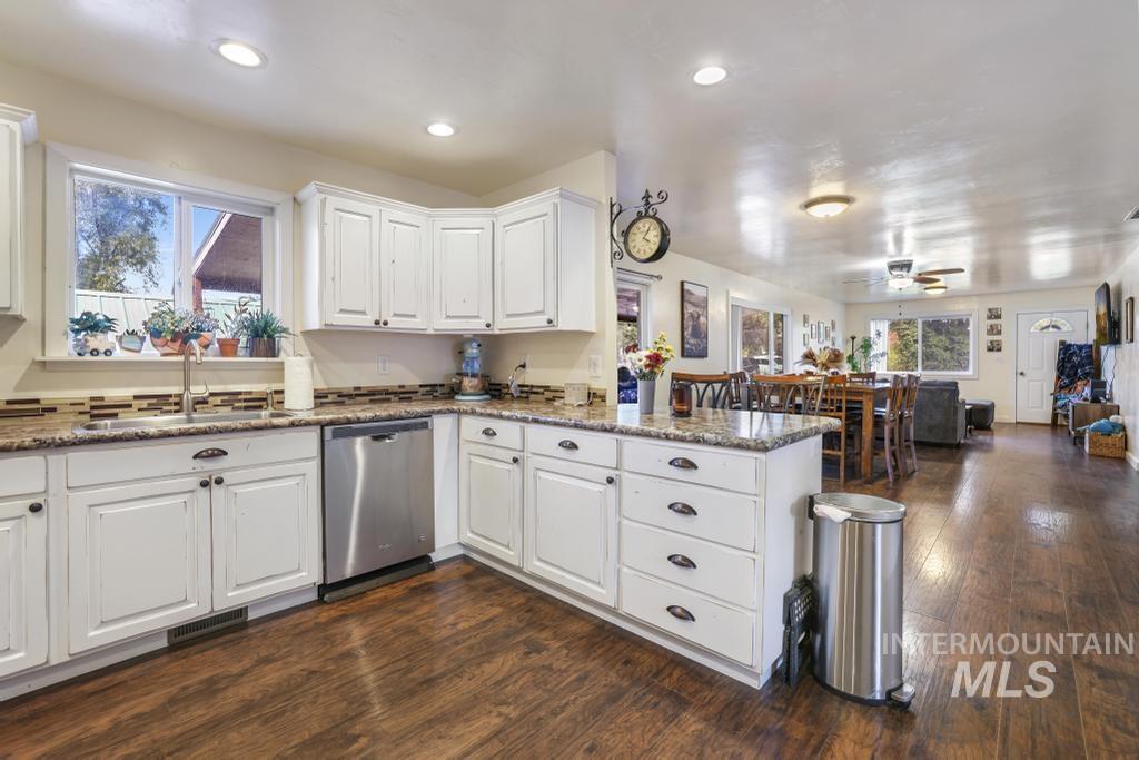 Kitchen with dark stone countertops, white cabinetry, dark wood-style floors, dishwasher, and a peninsula