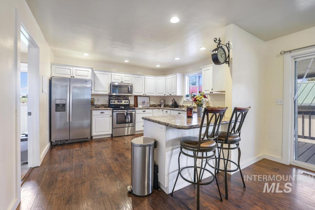 Kitchen featuring stainless steel appliances, a peninsula, white cabinets, recessed lighting, and dark wood finished floors