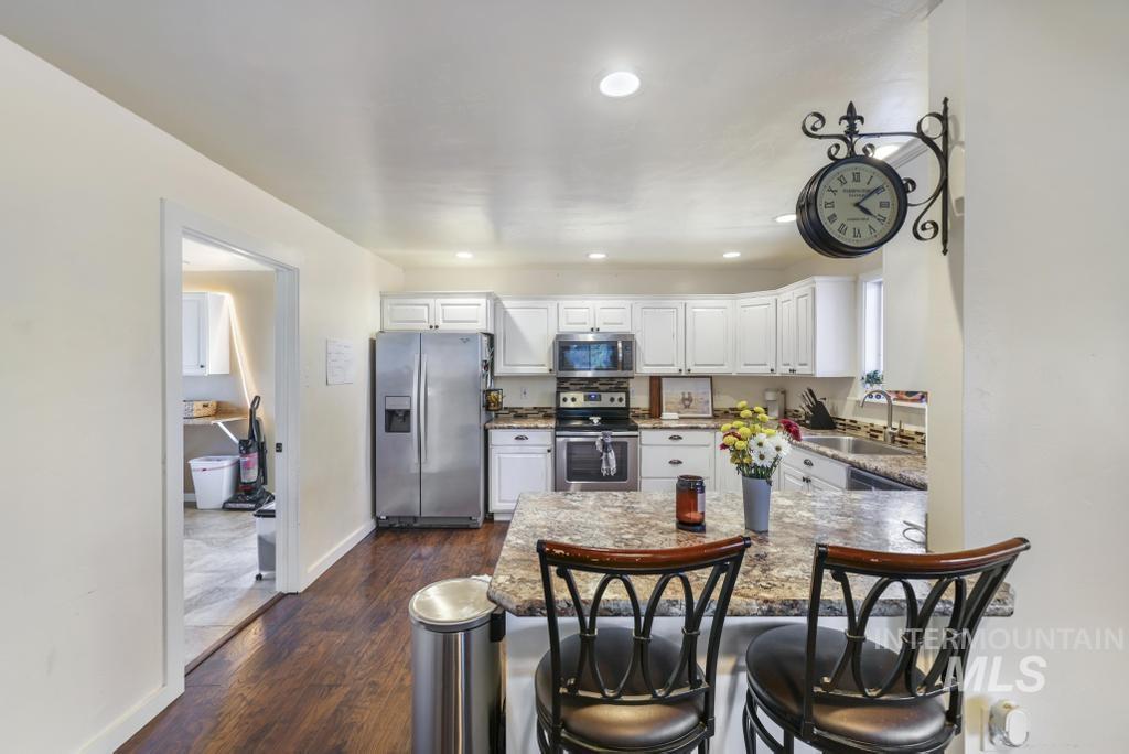 Kitchen featuring stainless steel appliances, white cabinets, a kitchen bar, dark wood-style flooring, and recessed lighting