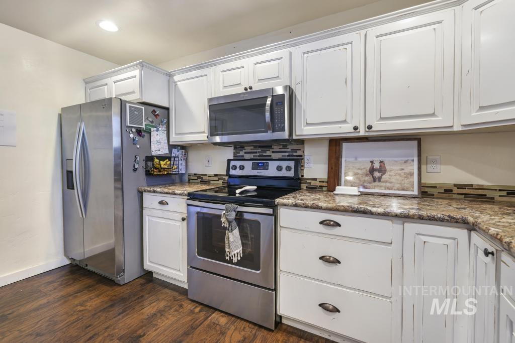 Kitchen featuring stainless steel appliances, white cabinets, dark stone countertops, and dark wood-style floors